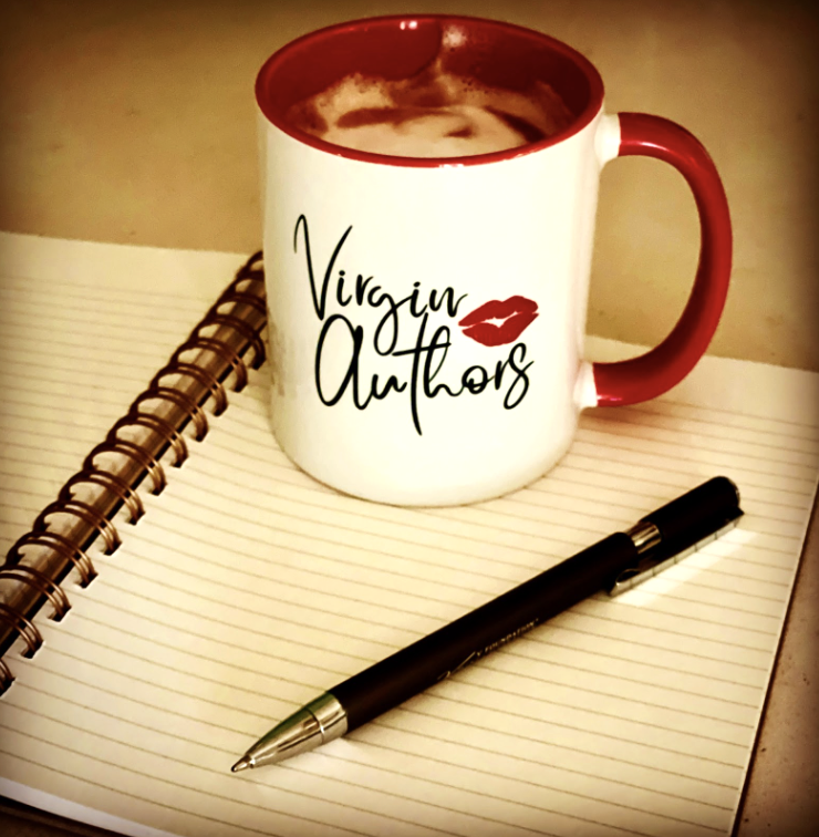 A white mug with red interior and handle, featuring the text 'Virgin Authors' with a lips graphic, placed next to an open spiral notebook and a black pen on a beige surface.