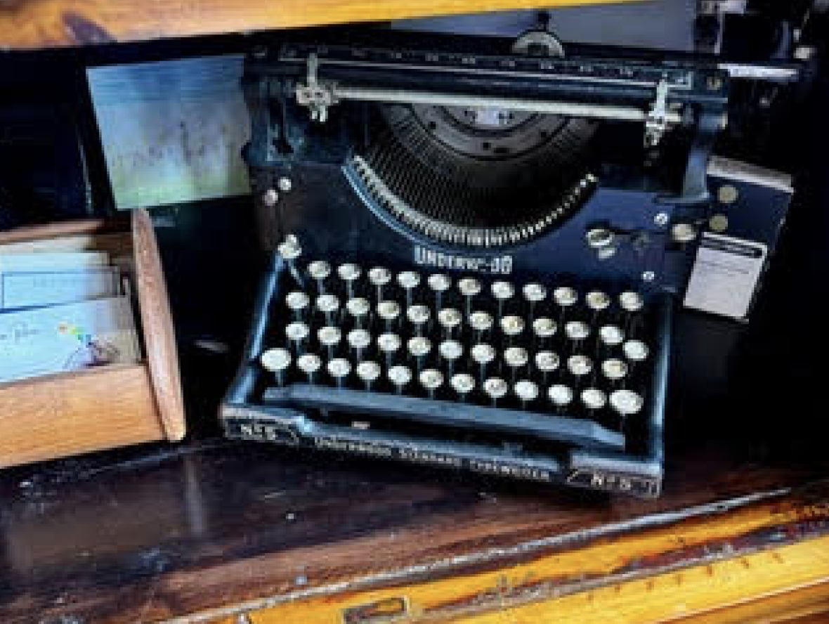 Vintage black typewriter on a wooden desk with a small wooden box to the left containing papers or index cards.