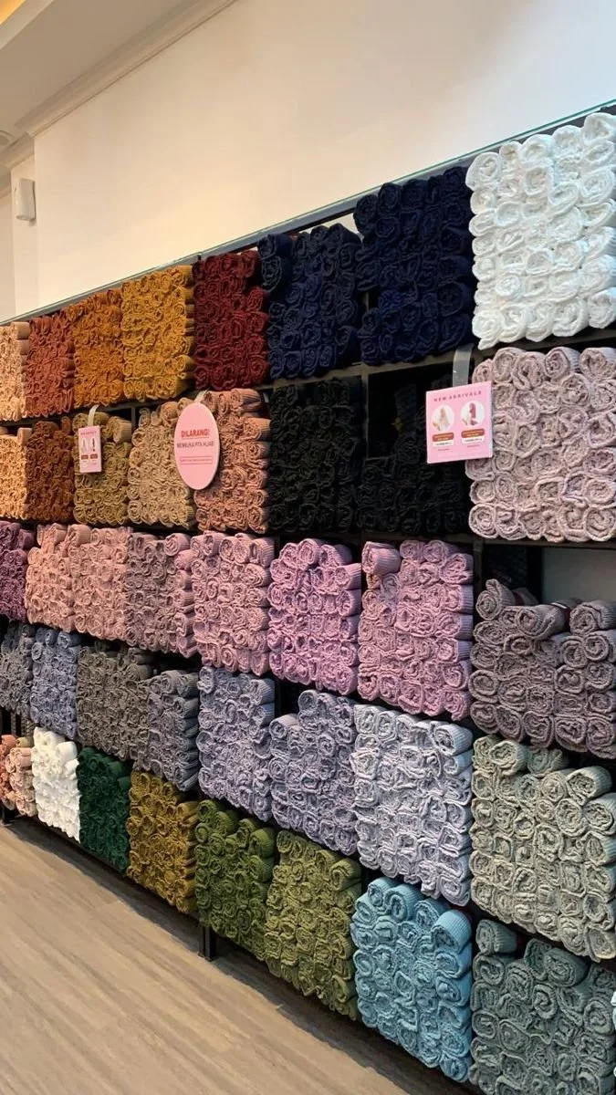 Display of neatly arranged rolled-up towels in various colors on a shelving unit in a home goods store.
