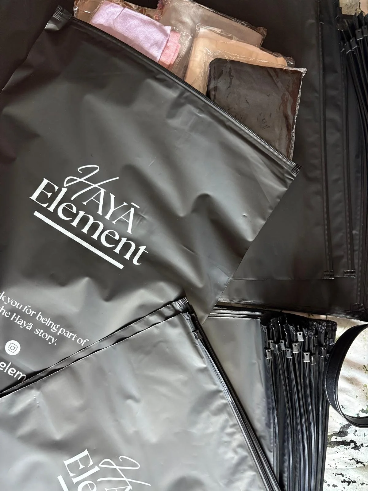 Black tote bags with the text 'Hayá Element' printed on them, along with some fabric samples and plastic bags containing fabric samples or swatches.