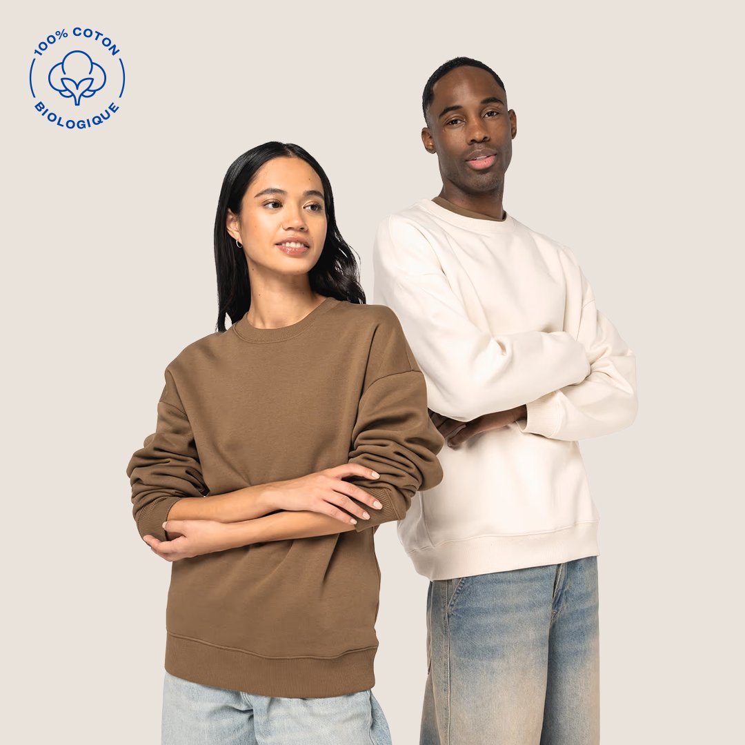 Deux jeunes adultes portent des sweatshirts et des pantalons décontractés, se tenant côte à côte. Logo en haut à gauche indiquant que le produit est 100% coton biologique.