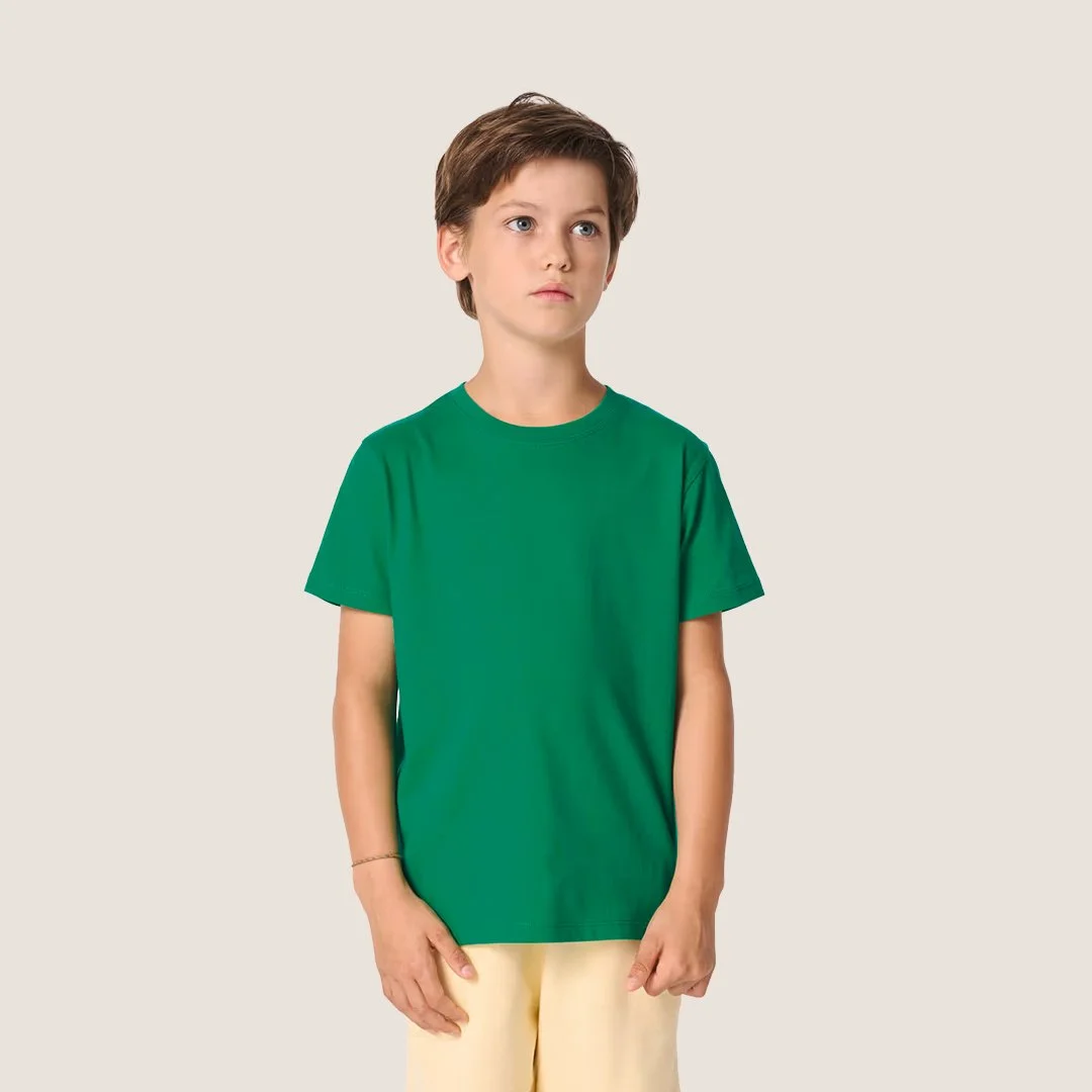 Jeune garçon aux cheveux bruns, portant un t-shirt vert et un pantalon clair, posé devant un fond neutre.