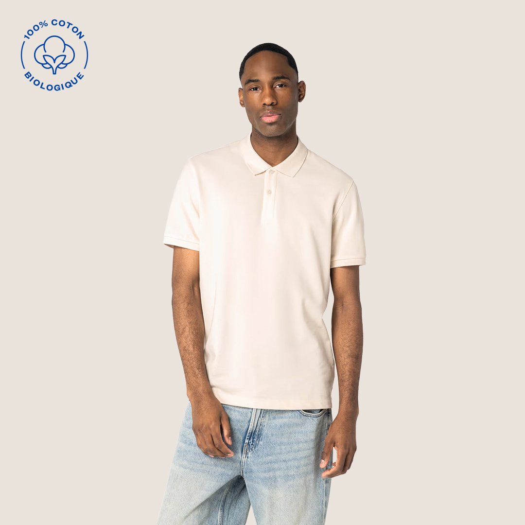 Un homme portant un polo blanc en coton biologique, debout contre un fond beige clair.