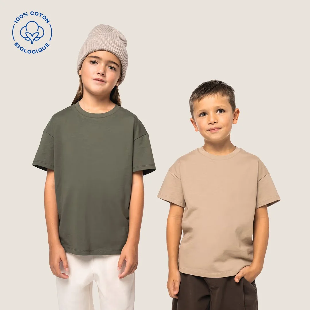 Deux enfants portent des t-shirts biologiques en coton à 100%, l'un en vert et l'autre en beige, avec un fond neutre.