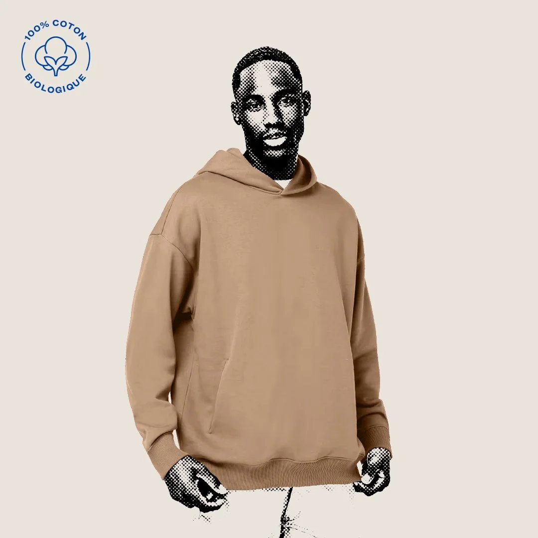 Courte description de l'image d'un homme portant un sweat à capuche beige, style graphique en noir et blanc sur le visage, fond clair, logo en haut à gauche indiquant '100% coton biologique'.
