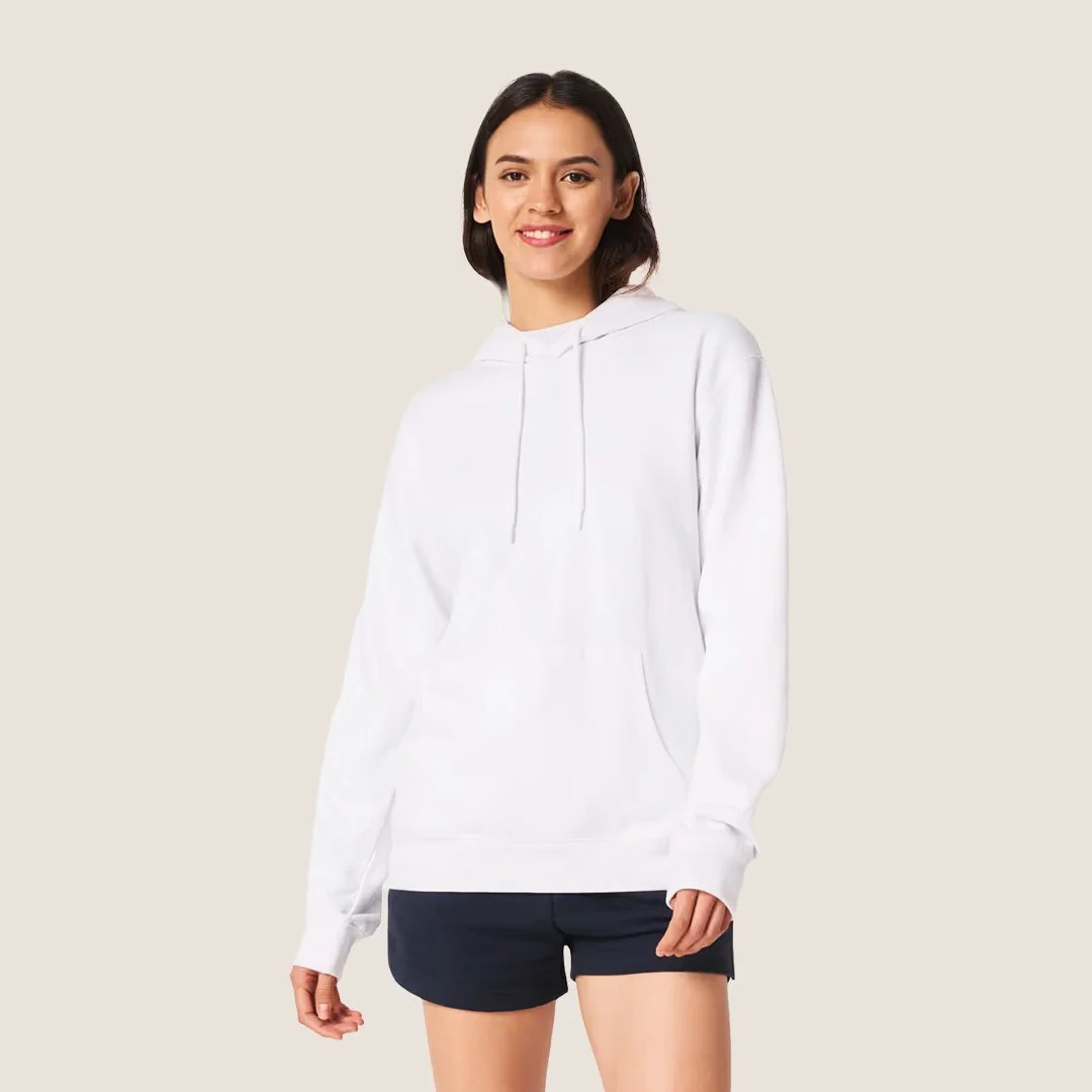 Une femme souriante porte un sweat à capuche blanc et un short noir, debout contre un fond beige.