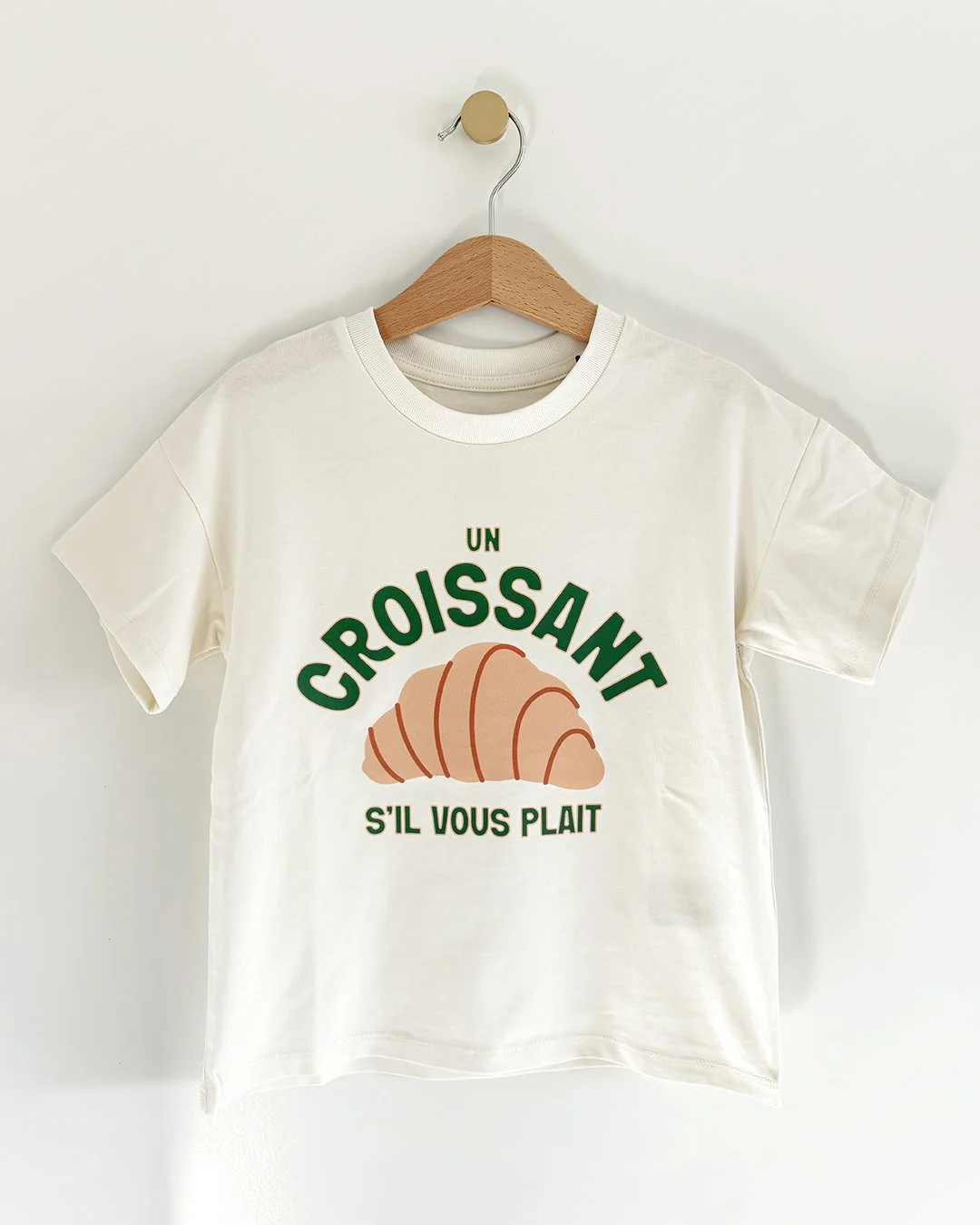 T-shirt blanc avec une illustration de croissant et le texte en français : "Un croissant s'il vous plaît".
