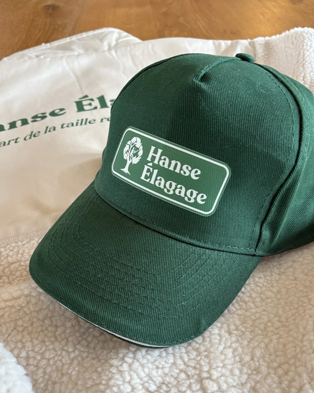 Casquette verte avec le logo 'Hanse Élagage' posée sur une couverture blanche.