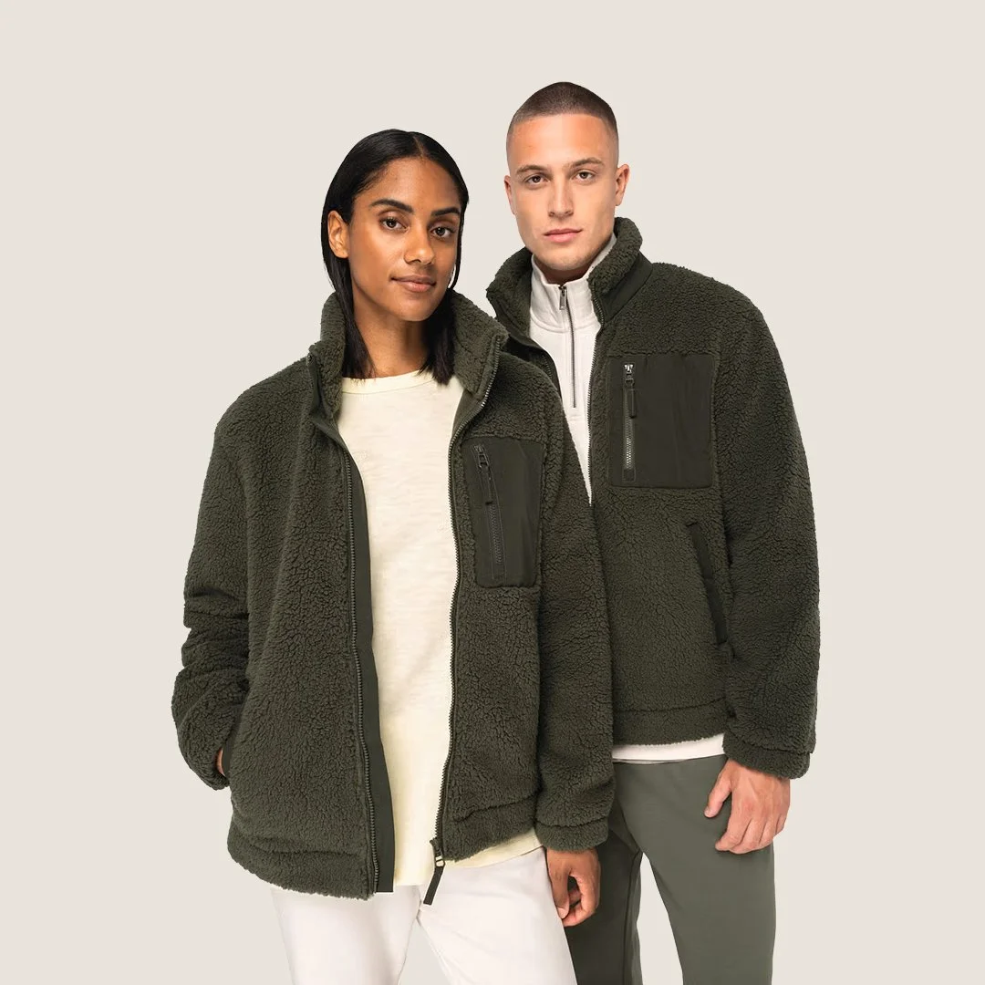 Deux personnes portant des vestes en polaire foncée posent contre un fond beige.