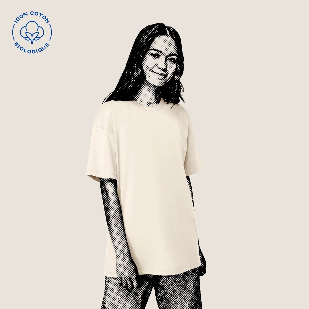 Une jeune femme souriante portant un t-shirt beige en coton biologique avec un symbole de coton 100% bio en haut à gauche de l'image.