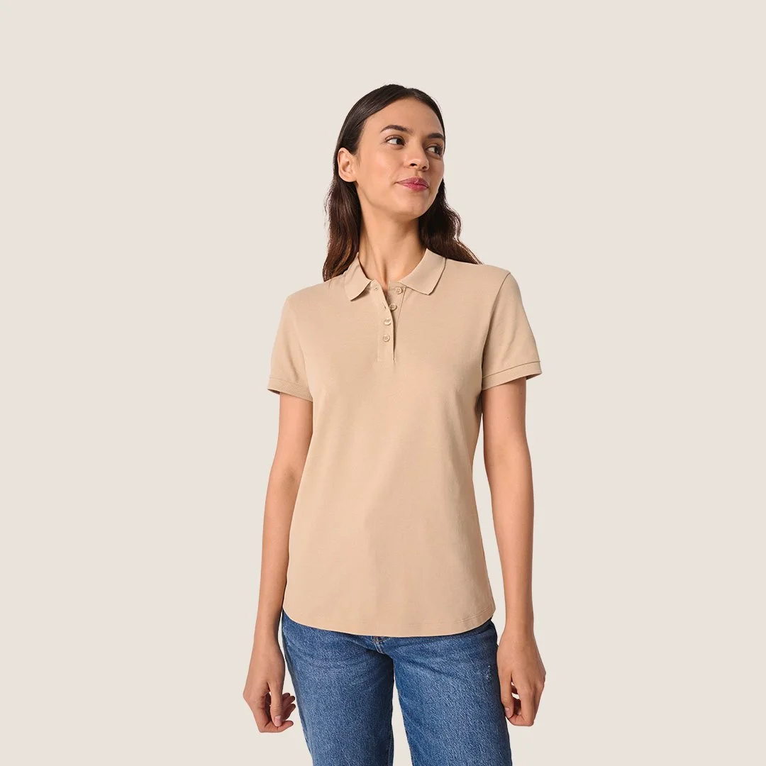 Femme portant un polo beige et un jean bleu clair. Fond neutre.