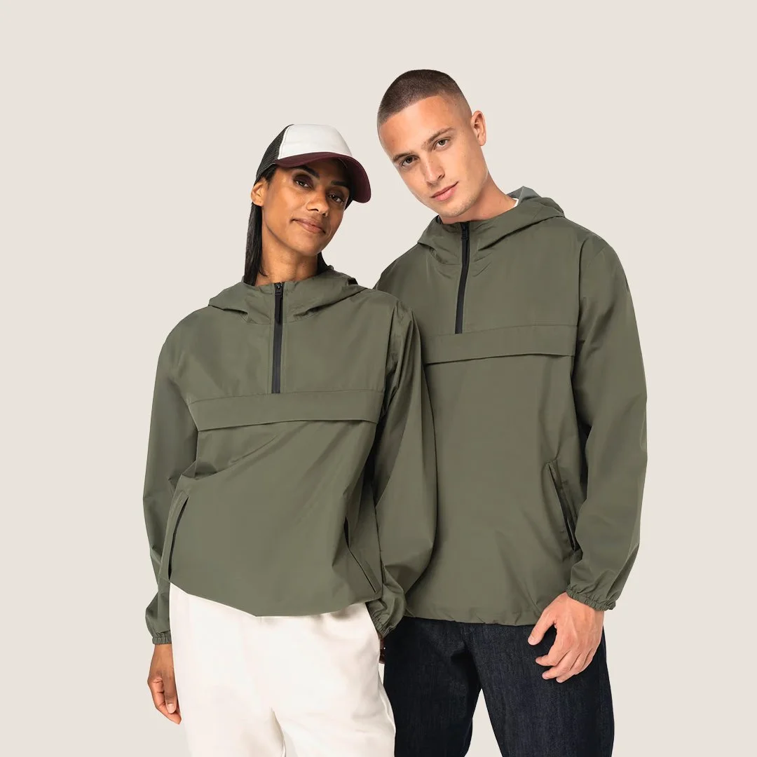 Deux personnes portent des vestes coupe-vent vert kaki, debout côte à côte contre un fond beige clair.