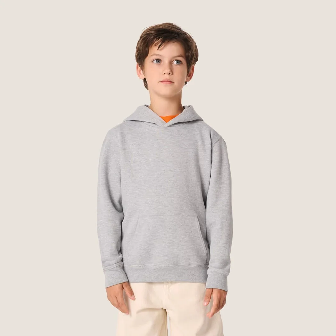 Jeune garçon portant un sweat à capuche gris clair, une chemise orange et un pantalon beige, debout contre un fond neutre.