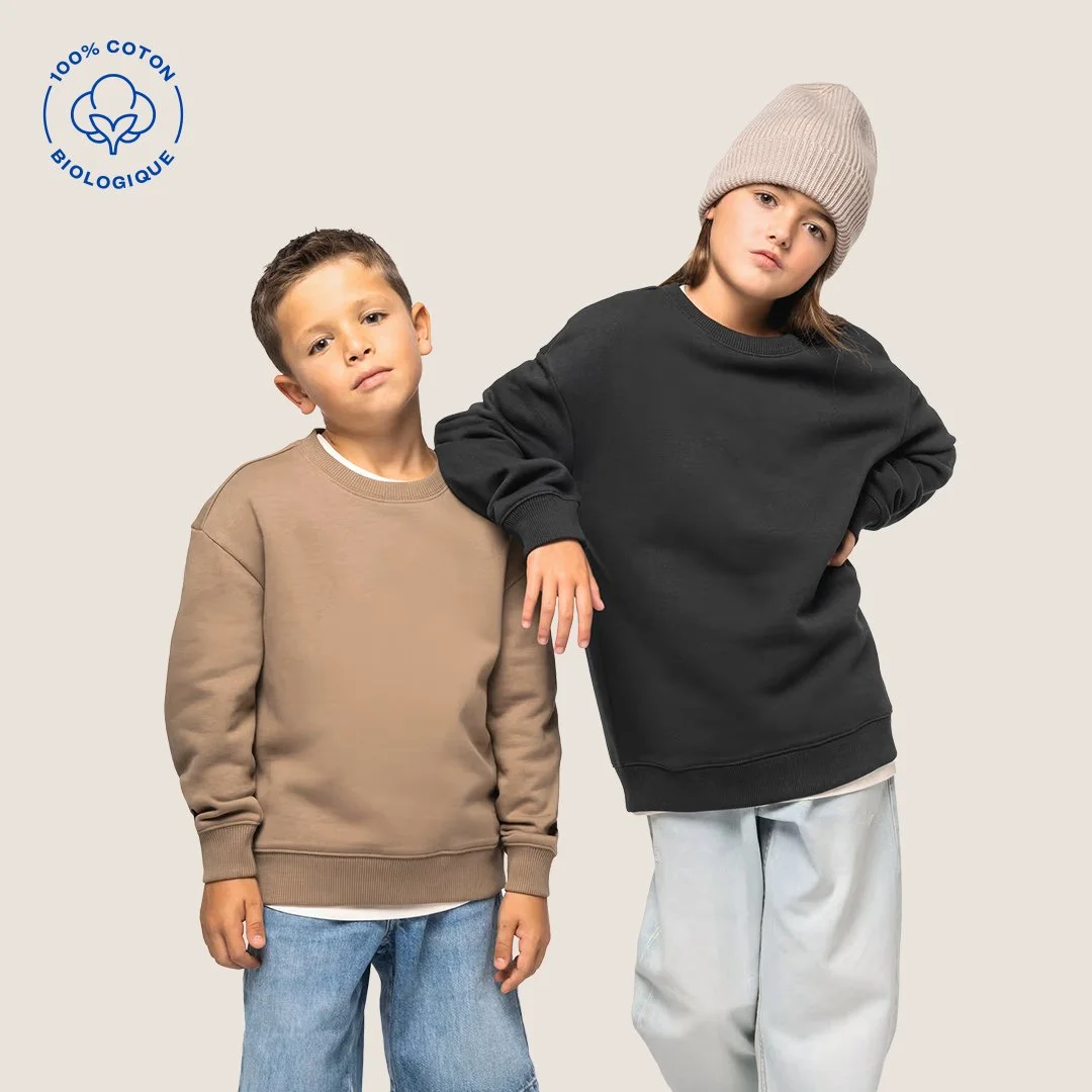 Deux enfants portant des sweats confortables, l'un beige et l'autre noir, avec un logo de coton biologique à gauche.