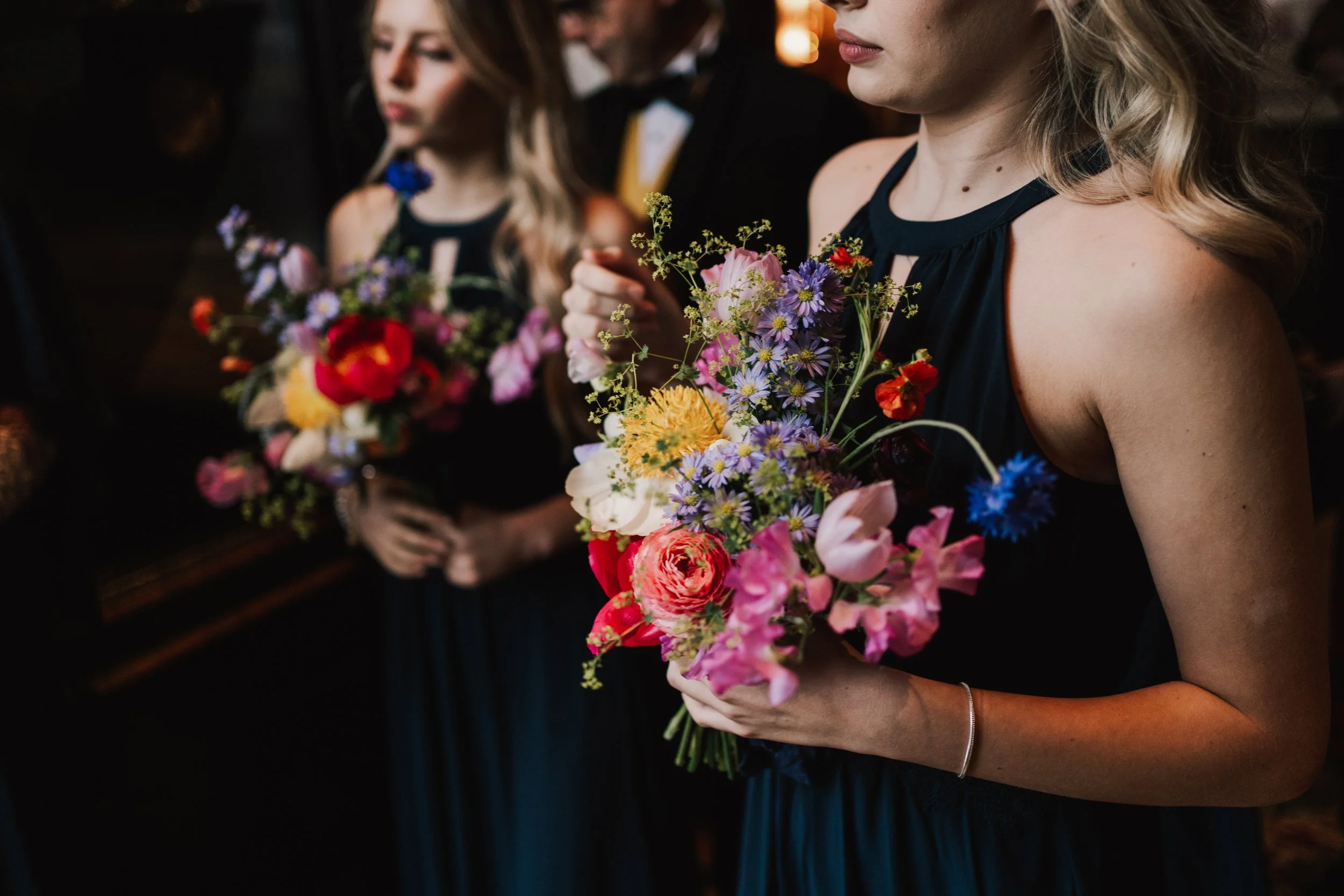 Bridesmaid in a navy blue dress holding colourful bridesmaid bouquet of flowers at a wedding at The Nomad Hotel, London.