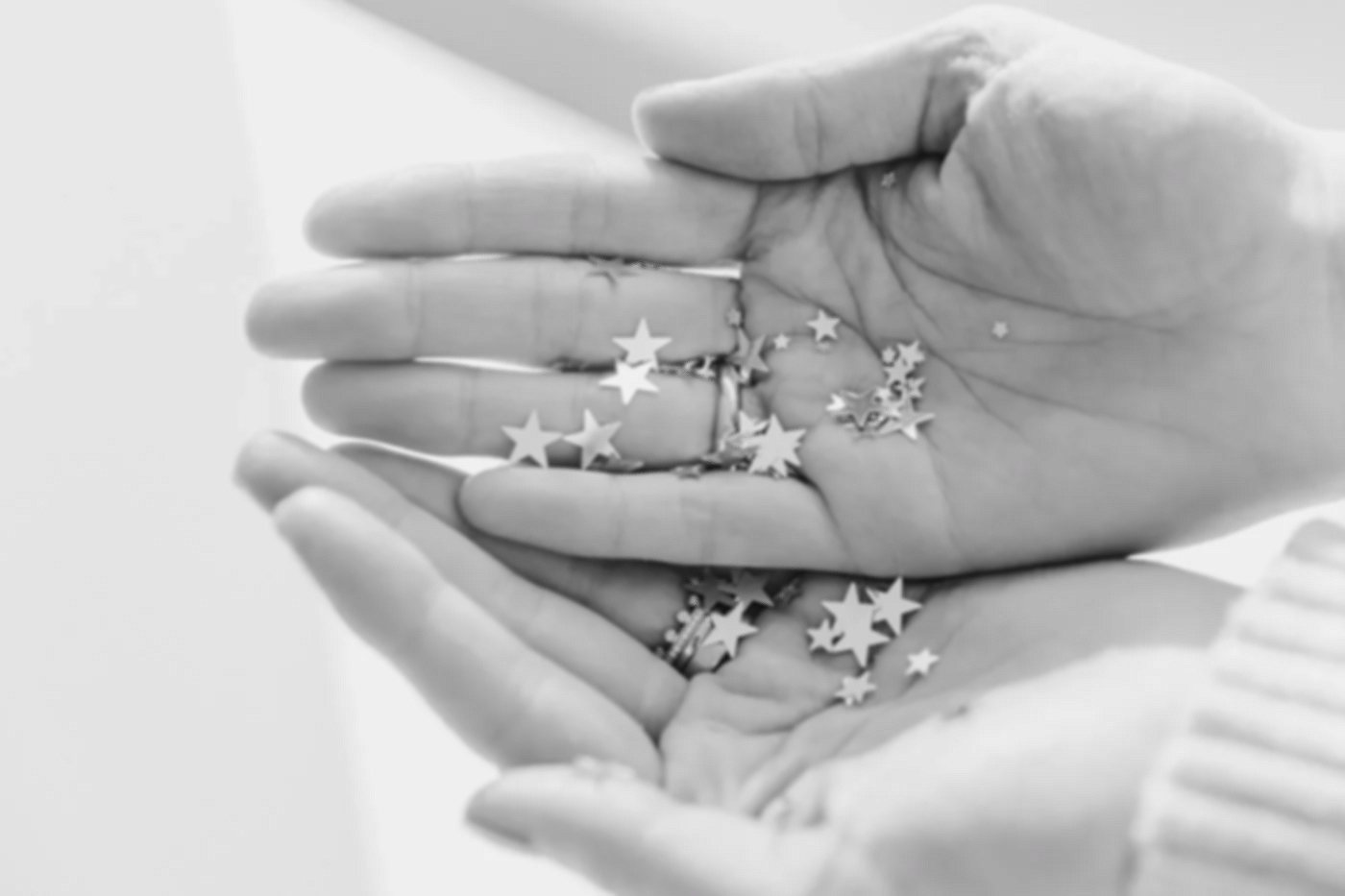 Nahaufnahme von Händen, die mit Sternchen dekoriert sind. Die Hände sind im schwarzen und weißen Foto sichtbar.