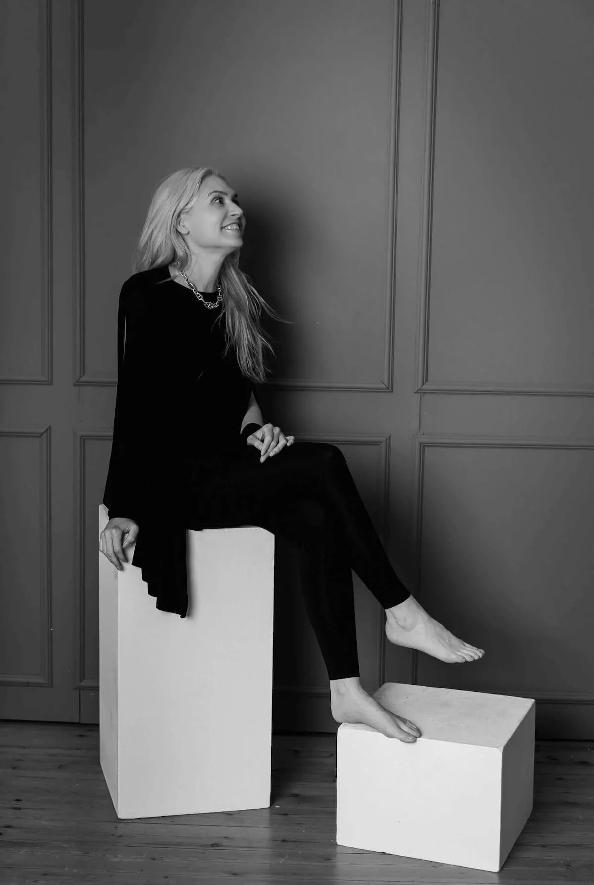 Merle Christin Mitsch sitzt auf einem Hocker vor einer Wand und blickt lächelnd nach oben