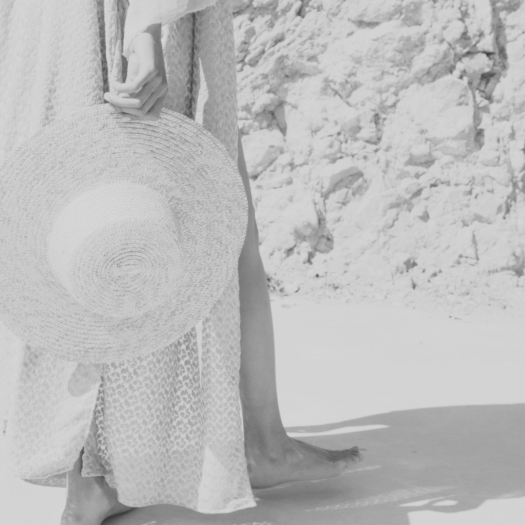 Merle Christin Mitsch steht barfuß im Sand und hält einen runden Strohhut in der Hand