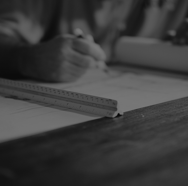 Close-up of a person's hand writing with a pen on paper, with a ruler on the desk in black and white.