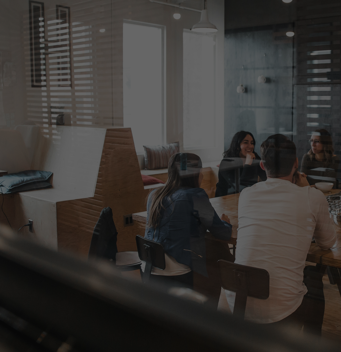 Group of five people sitting at a wooden table in a modern, well-lit room, engaging in conversation and smiling.