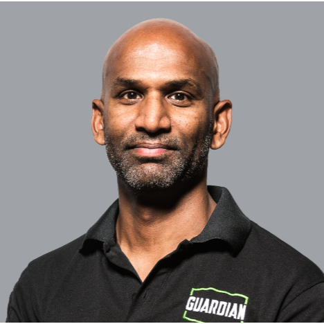 Portrait of a man with a bald head and beard wearing a black collared shirt with a Guardian logo