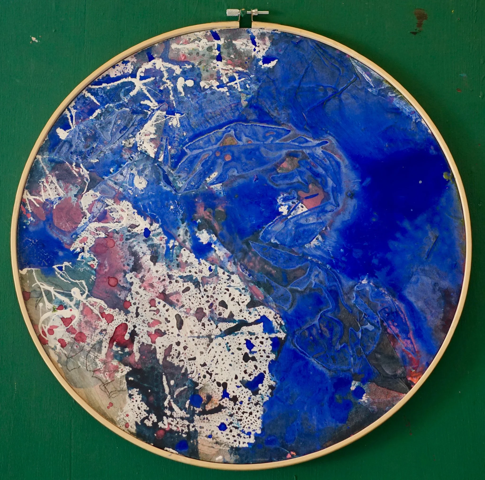 Abstrakte Gemälde mit blauen, weißen und roten Farben, in einem runden Rahmen auf grünem Hintergrund.