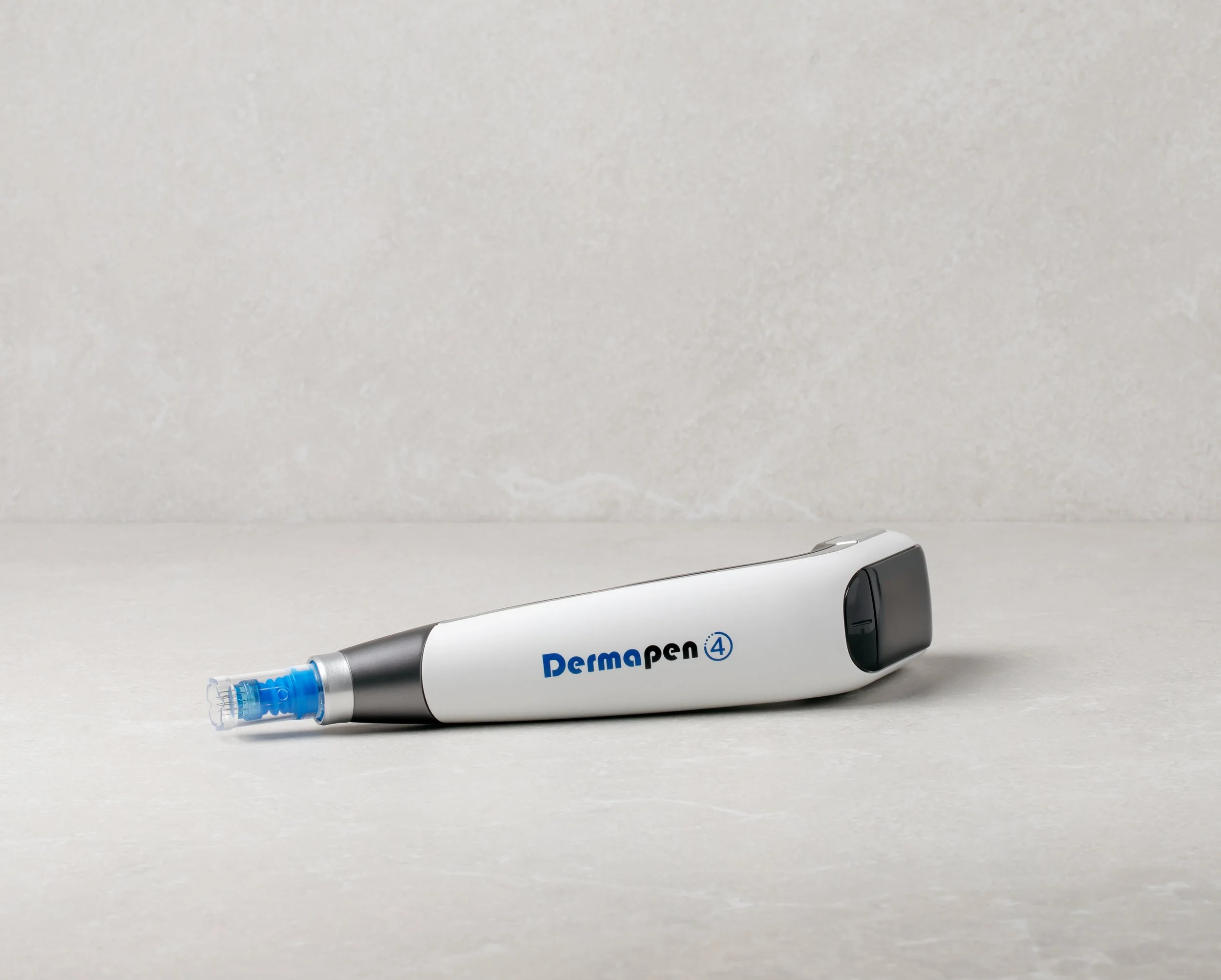 A white Derma pen 4 device with a blue needle tip resting on a light gray surface against a beige wall background.