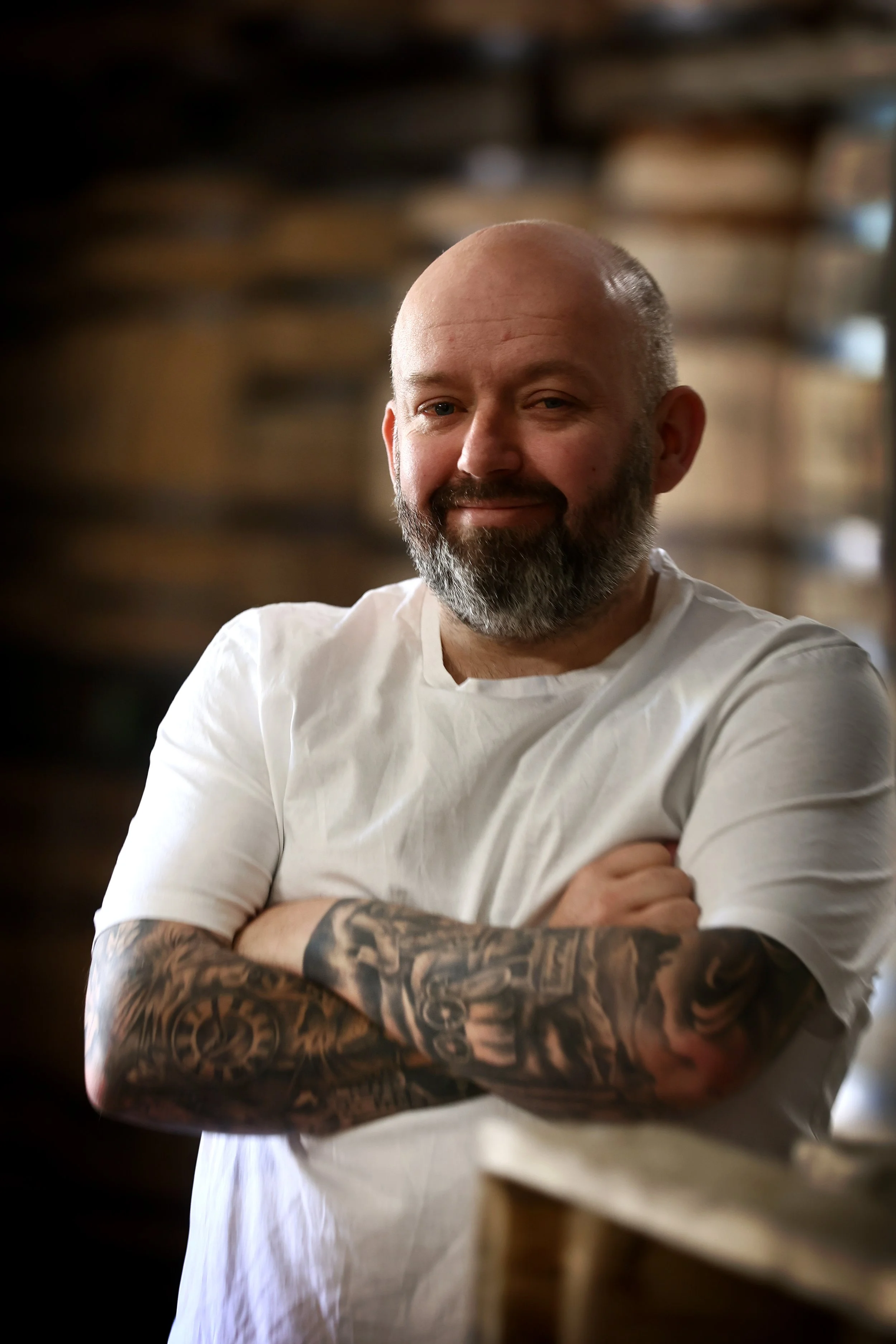 Managing Director of Oakwood Cooperage, Brent Bowie, wearing a white t-shirt, standing with arms crossed and smiling in front of casks.