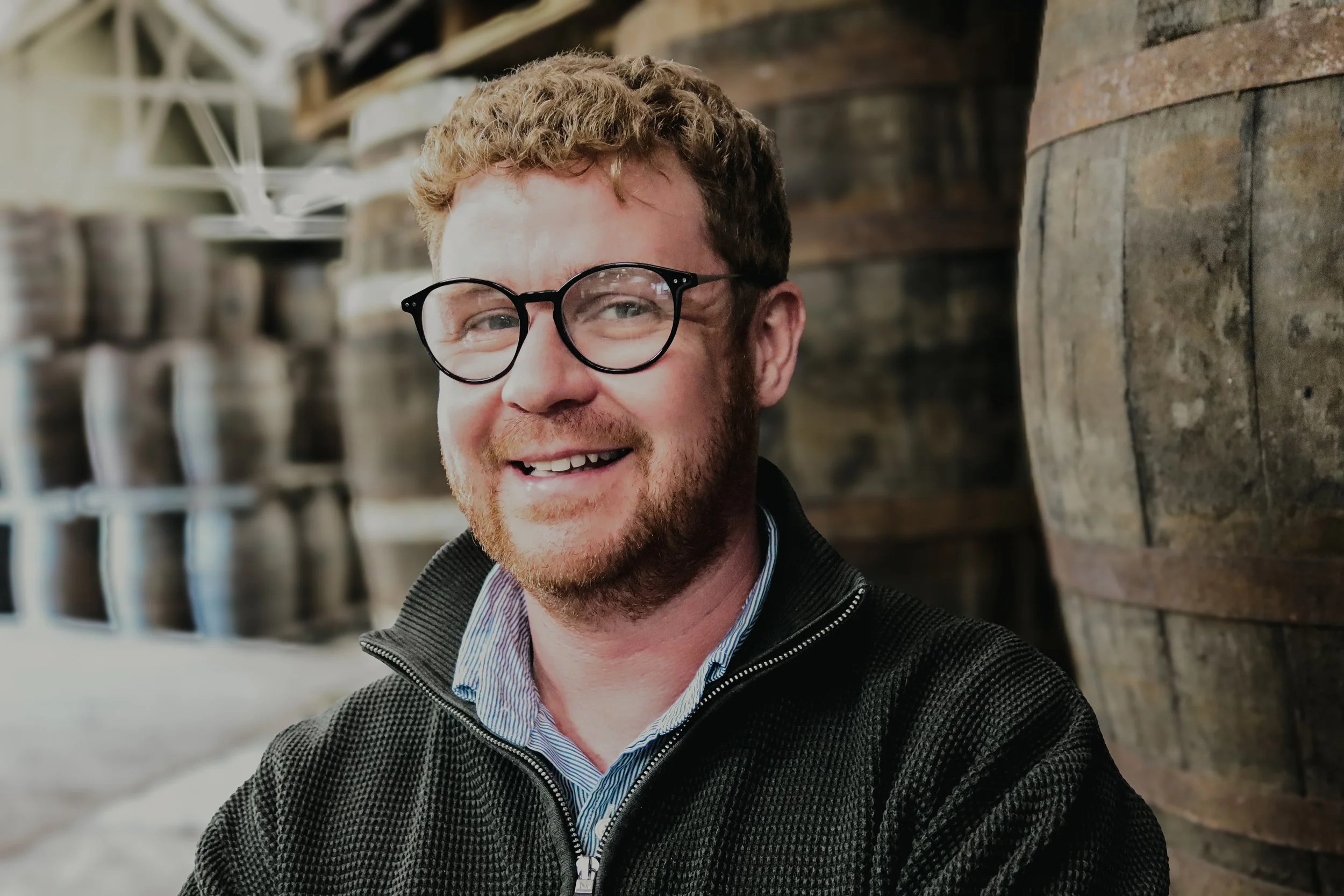 A portrait of Ryen Gardiner standing in front of some casks