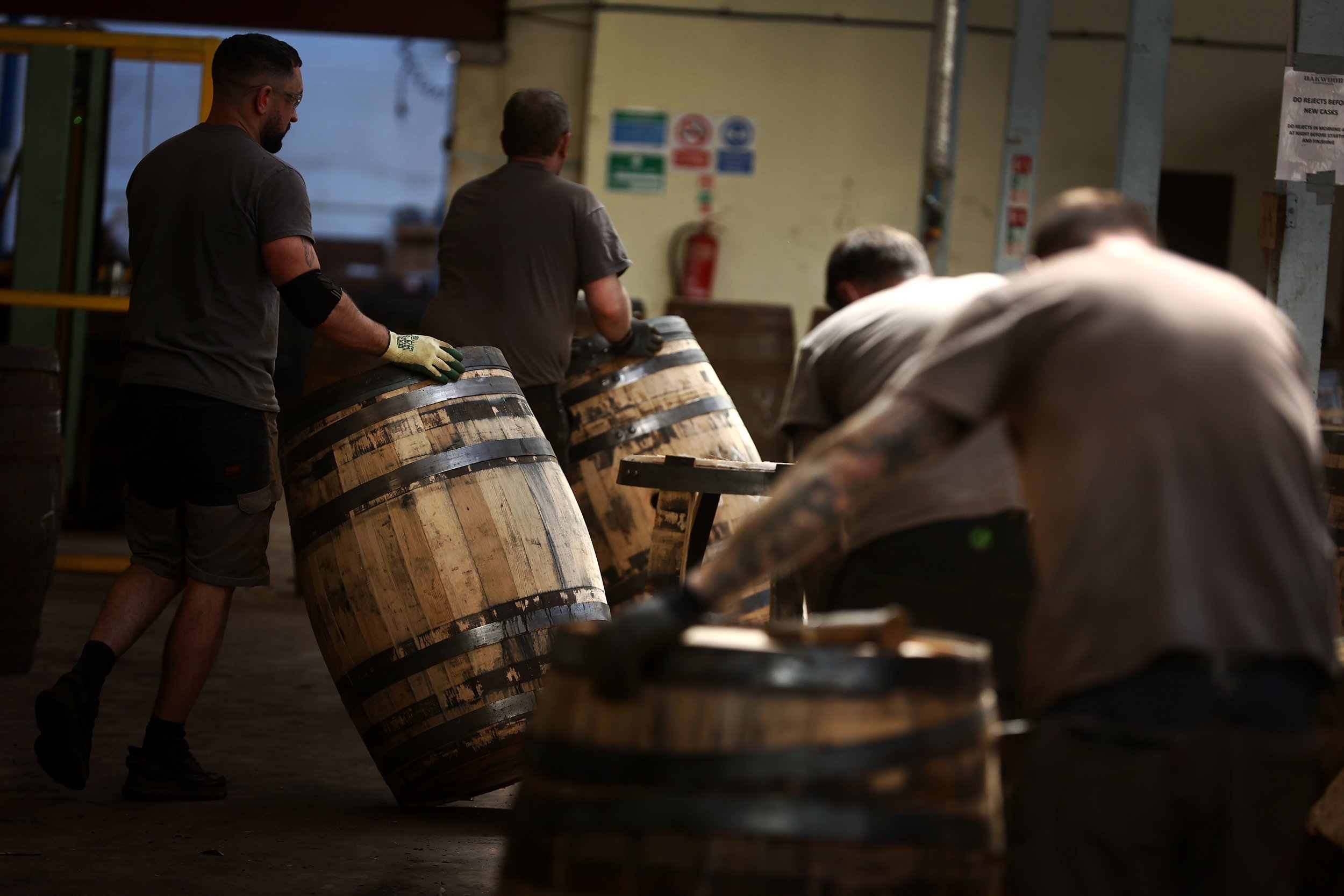 Four male coopers moving barrels by hand through the cooperage