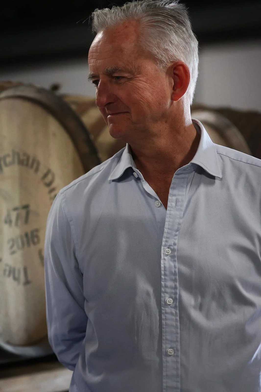 Chairman of Oakwood Cooperage, Graham Hamilton, standing in a whisky warehouse with wooden barrels stacked on shelves.
