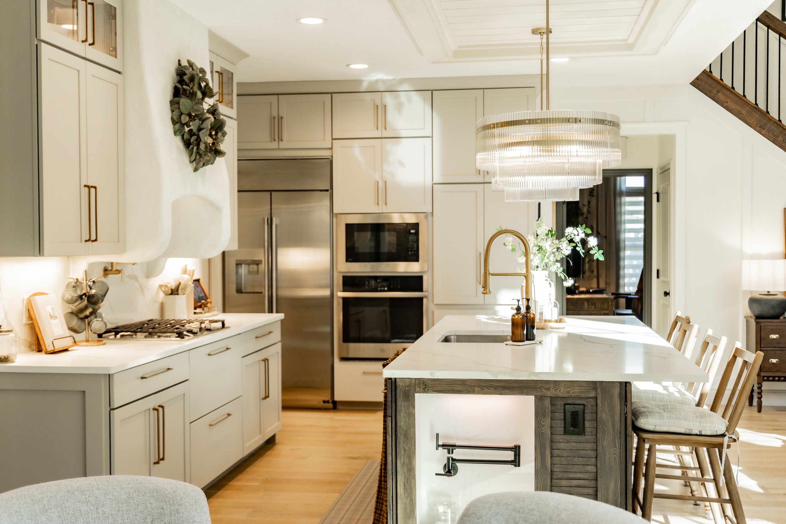 Bright, modern kitchen with white cabinets, stainless steel appliances, a large island with bar stools, and a decorative chandelier overhead.