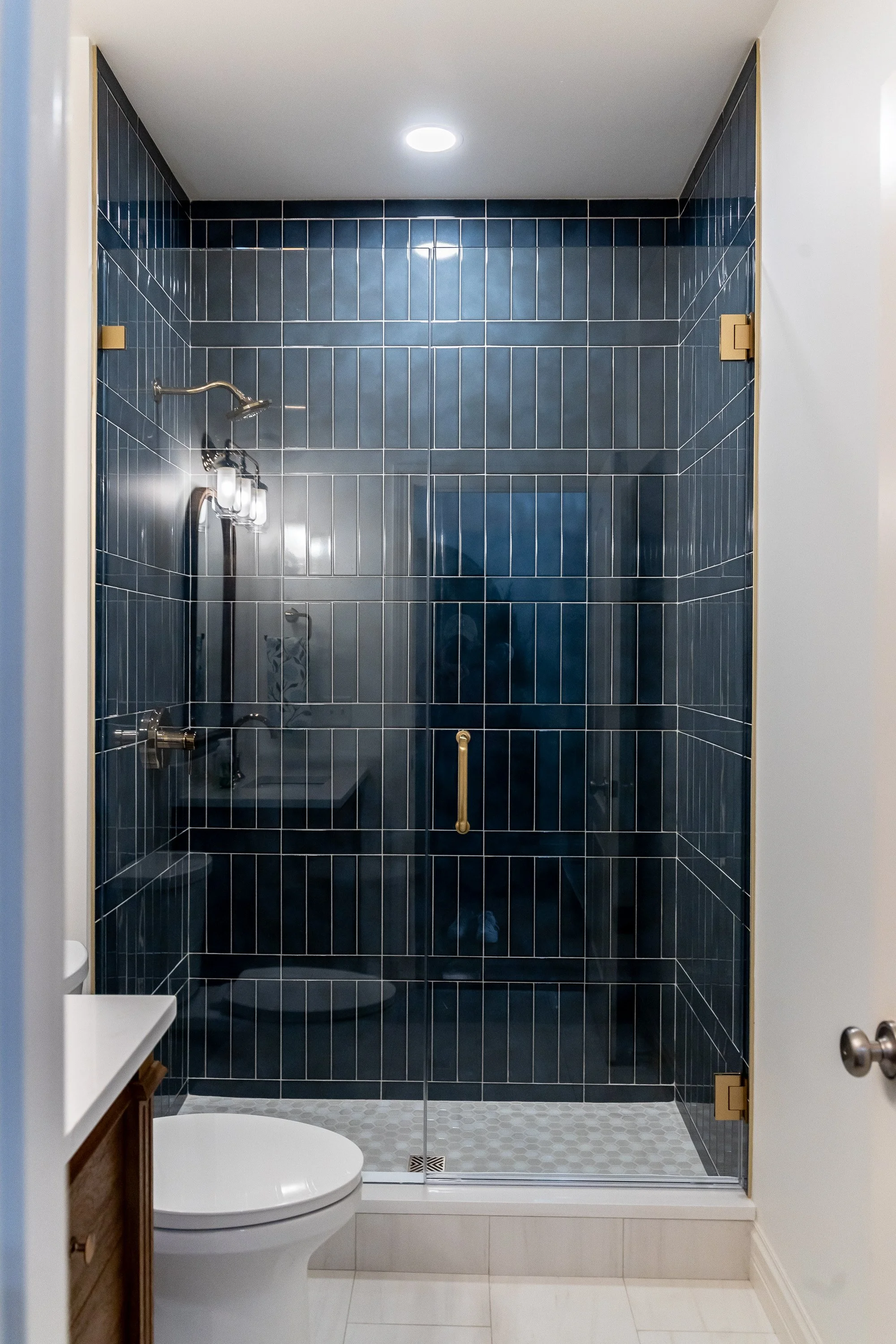 Walk-in shower with floor-to-ceiling blue vertical tile and frameless glass enclosure with gold hardware