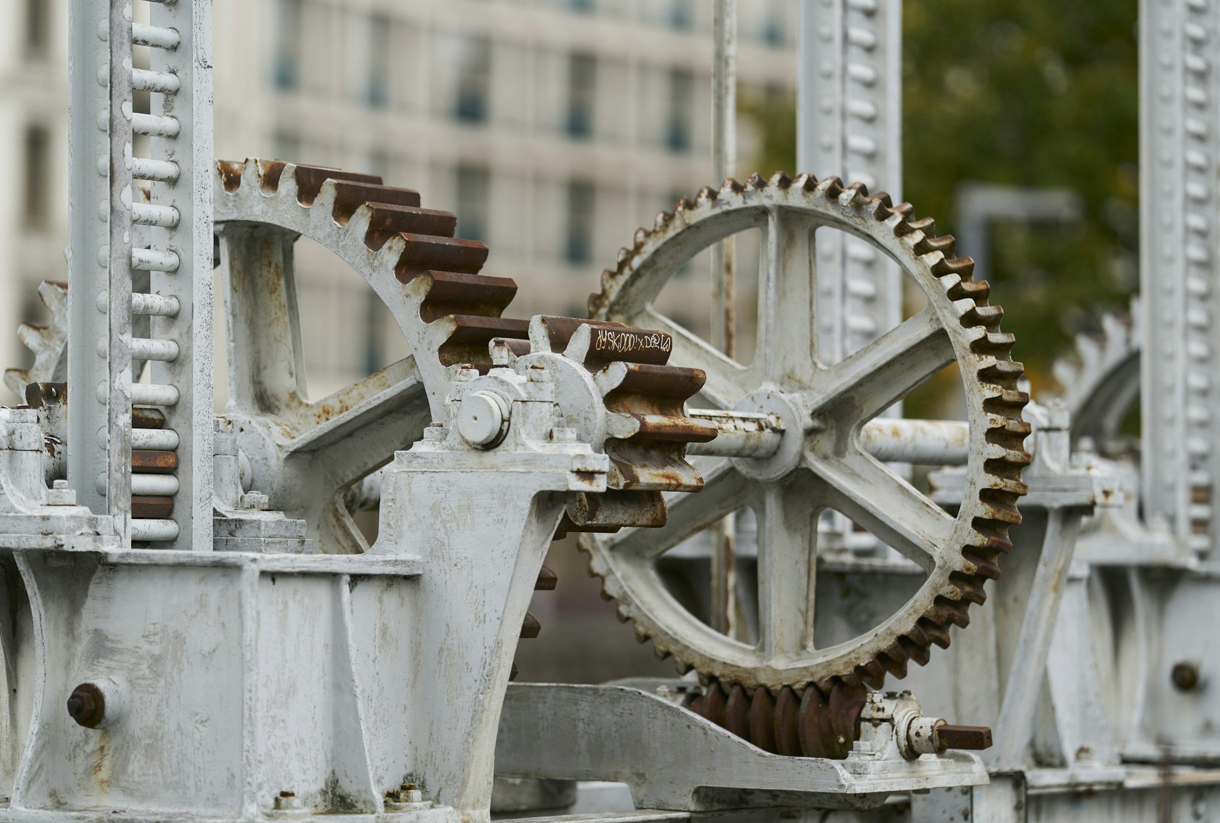 Close-up of vintage metal gears and machinery with rust, outdoors in an urban setting.