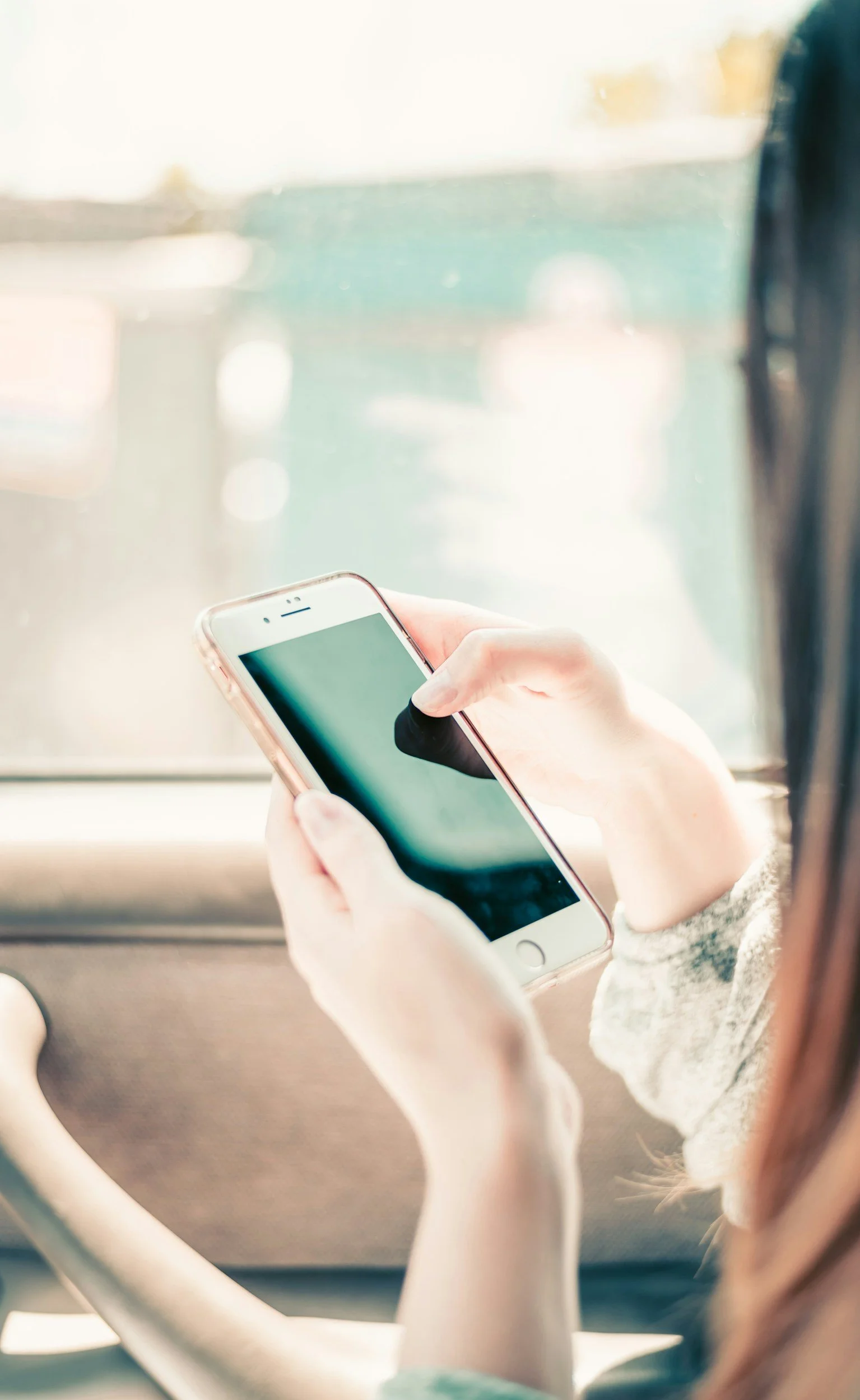 Person using smartphone inside a vehicle, with a blurred view of the outside through the window