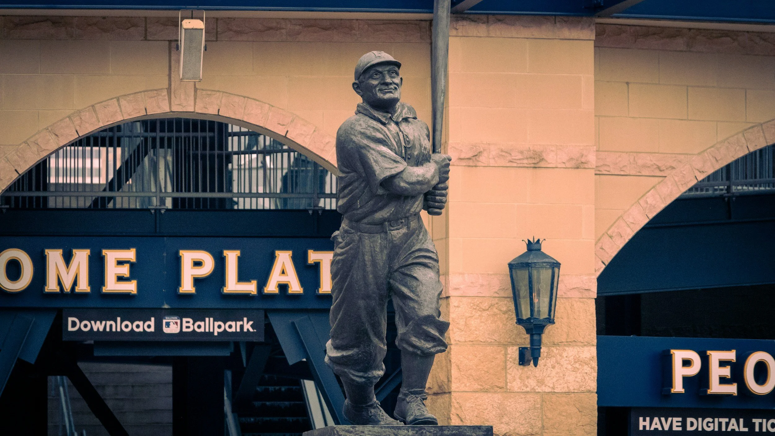 A statue of a young baseball player holding a bat, standing in front of a building with the sign 'Home Plate' and a light fixture.