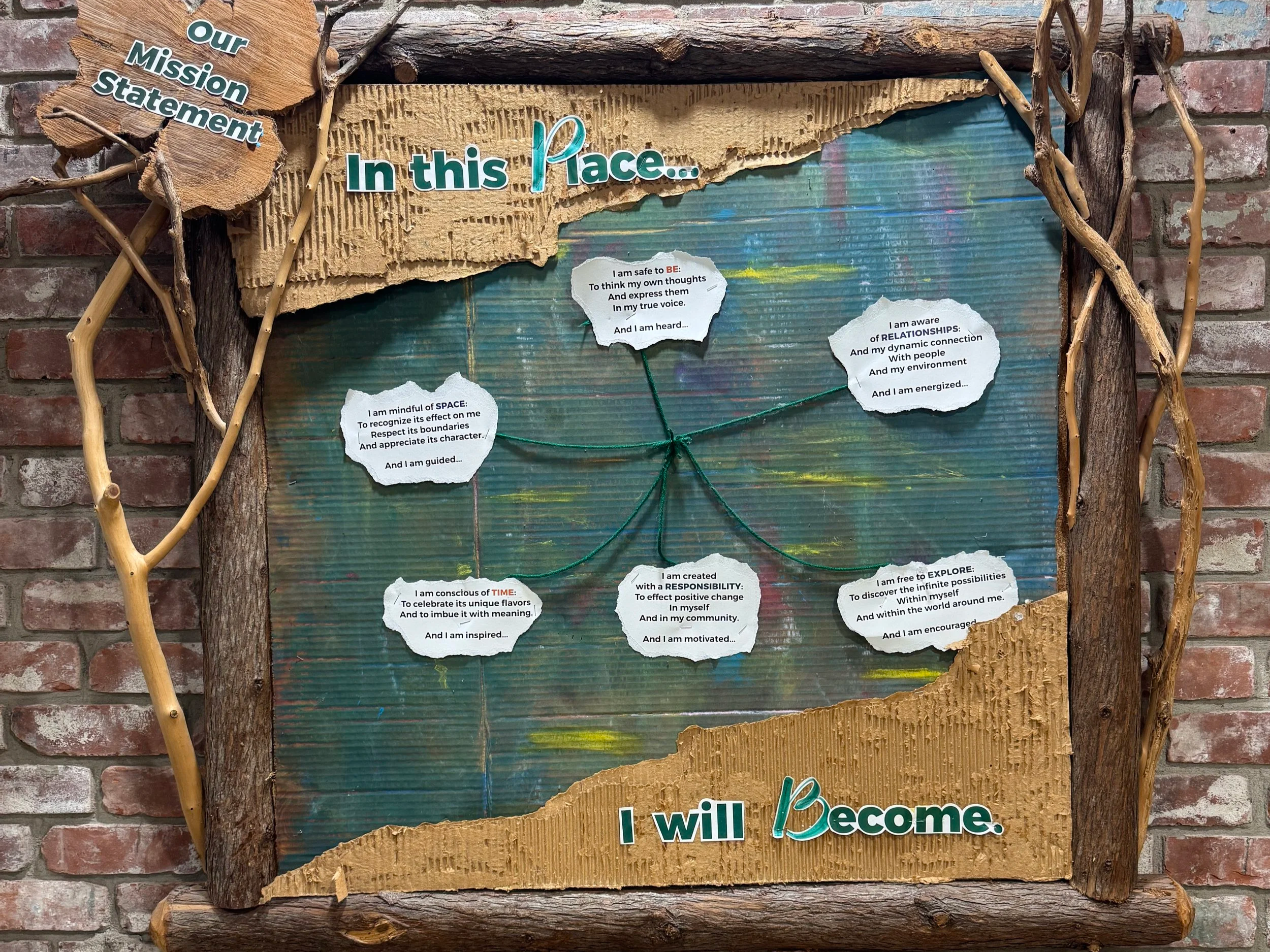 A decorative display on a wall with a wooden frame and textured background, featuring mission statement text and signed affirmations about personal growth and relationships.