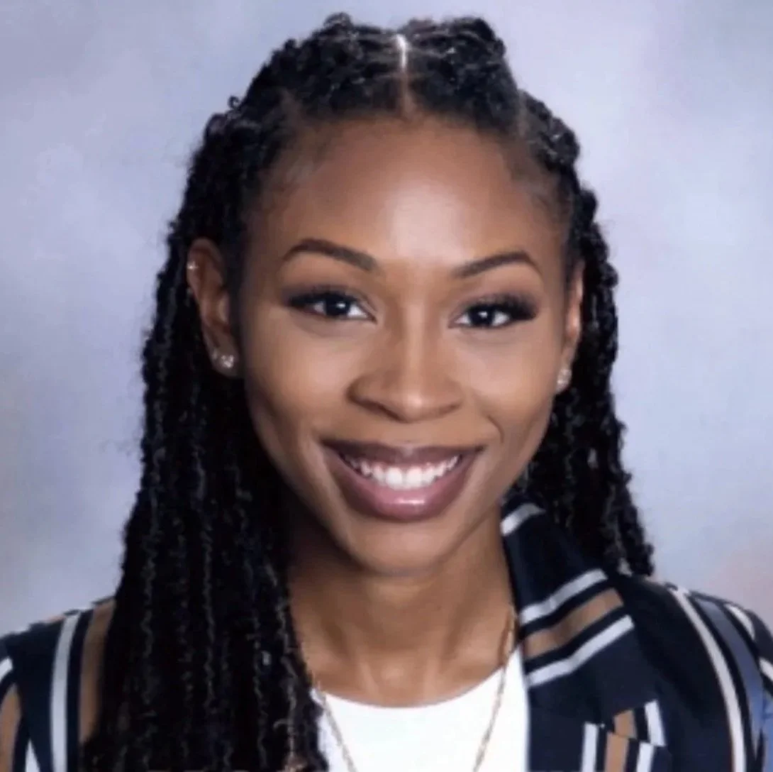 Smiling woman with dreadlocks, wearing a striped shirt, earrings, and a necklace.
