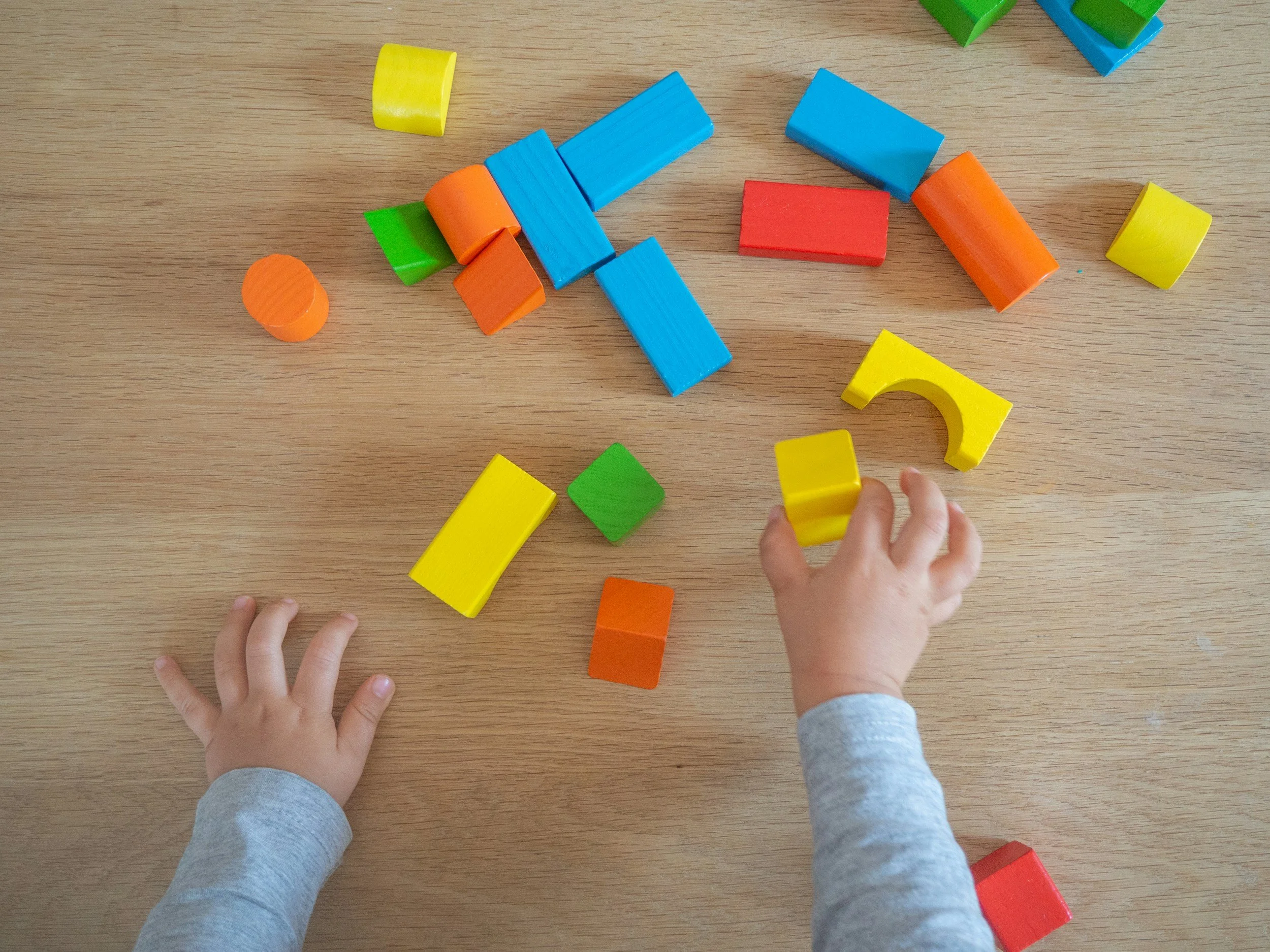 Child's hands playing with colorful wooden building blocks scattered on a wooden surface.