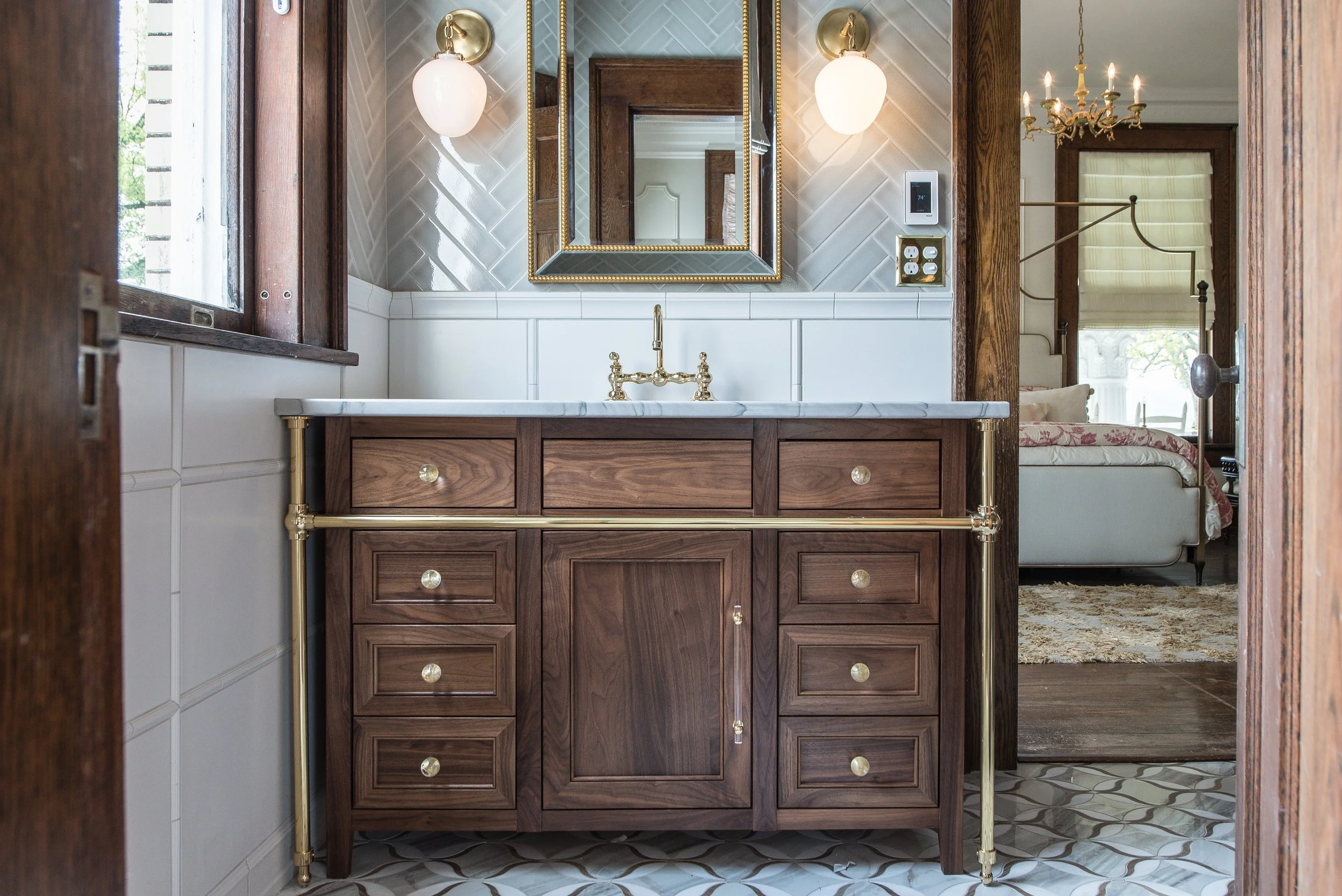 A bathroom vanity with a wooden cabinet, marble countertop, gold fixtures, and a mirror above, with wall-mounted lights flanking the mirror.