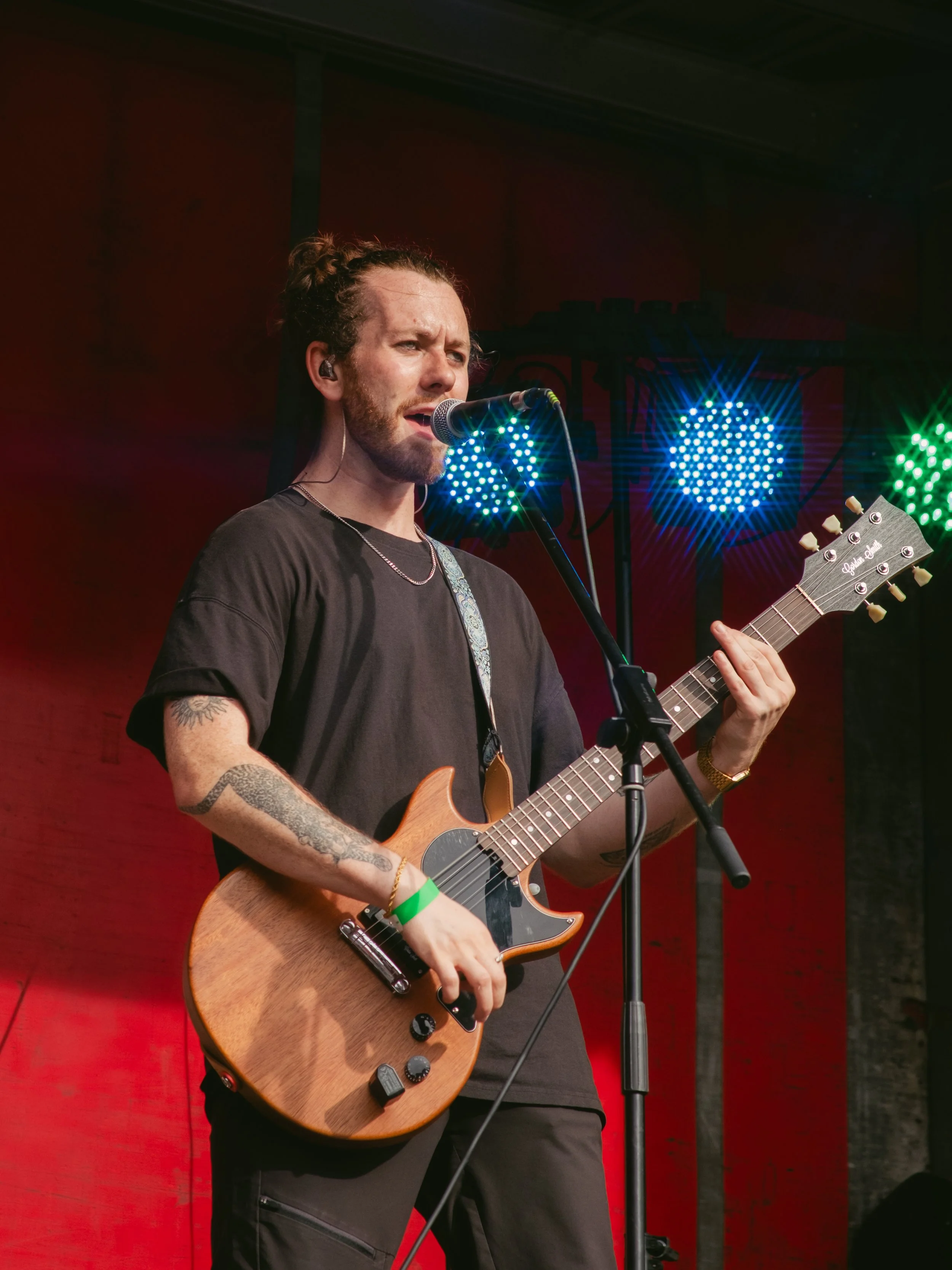 A male musician performing on stage with a guitar, singing into a microphone, with colorful stage lights in the background.