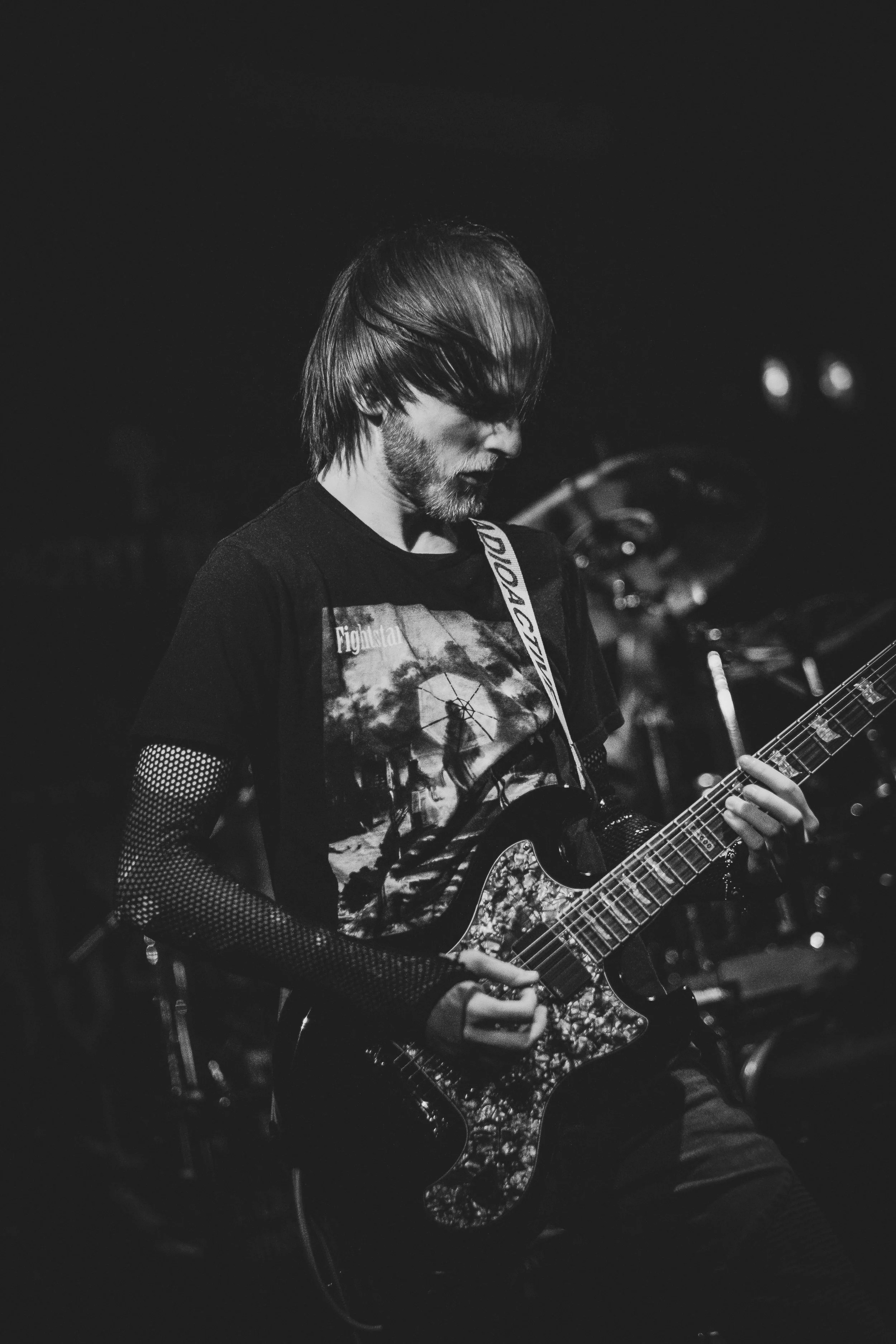A man playing an electric guitar on stage at night, shown in black and white.