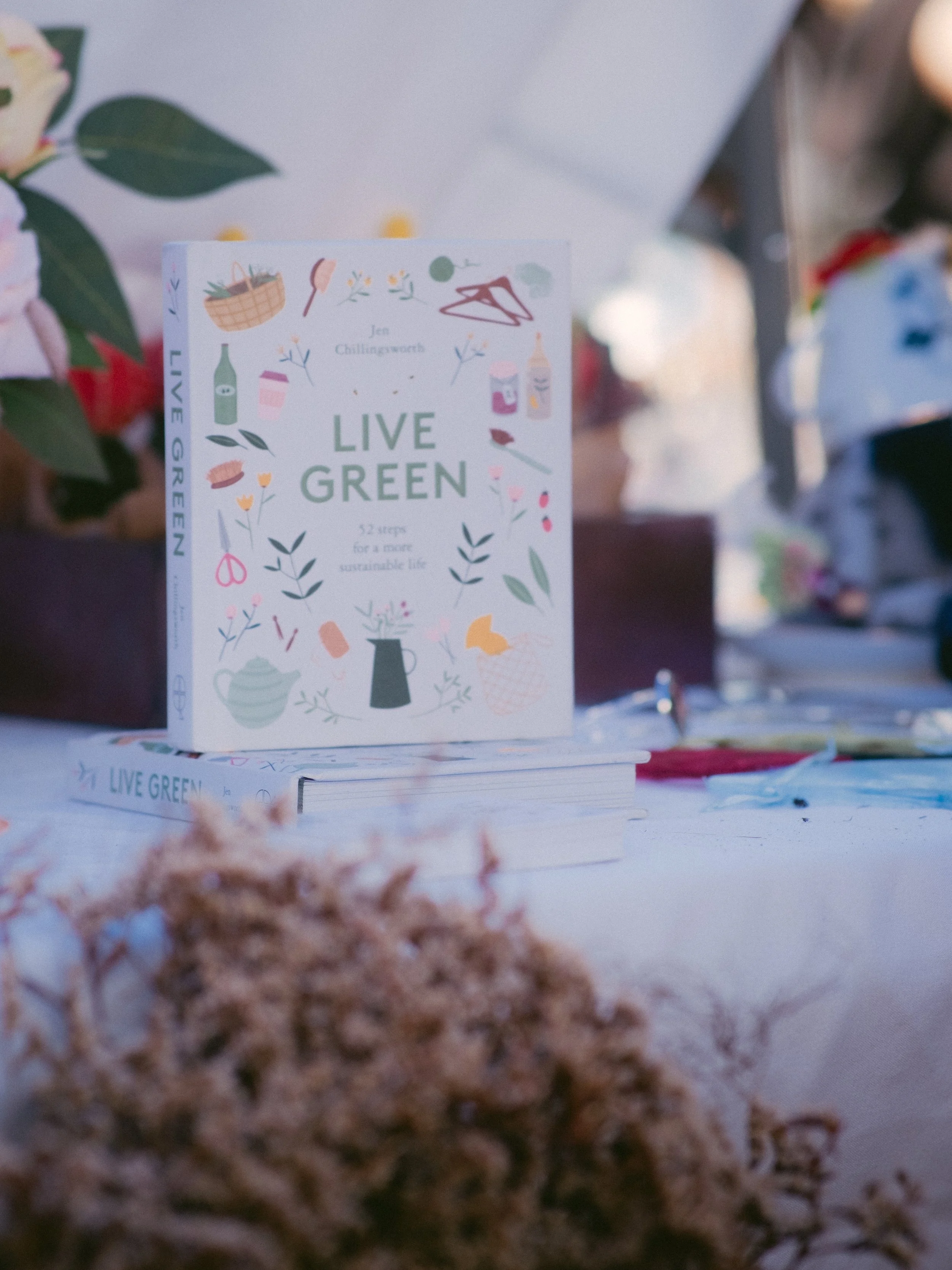 A book titled 'Live Green' displayed on a table with plants and flowers, promoting a sustainable lifestyle.