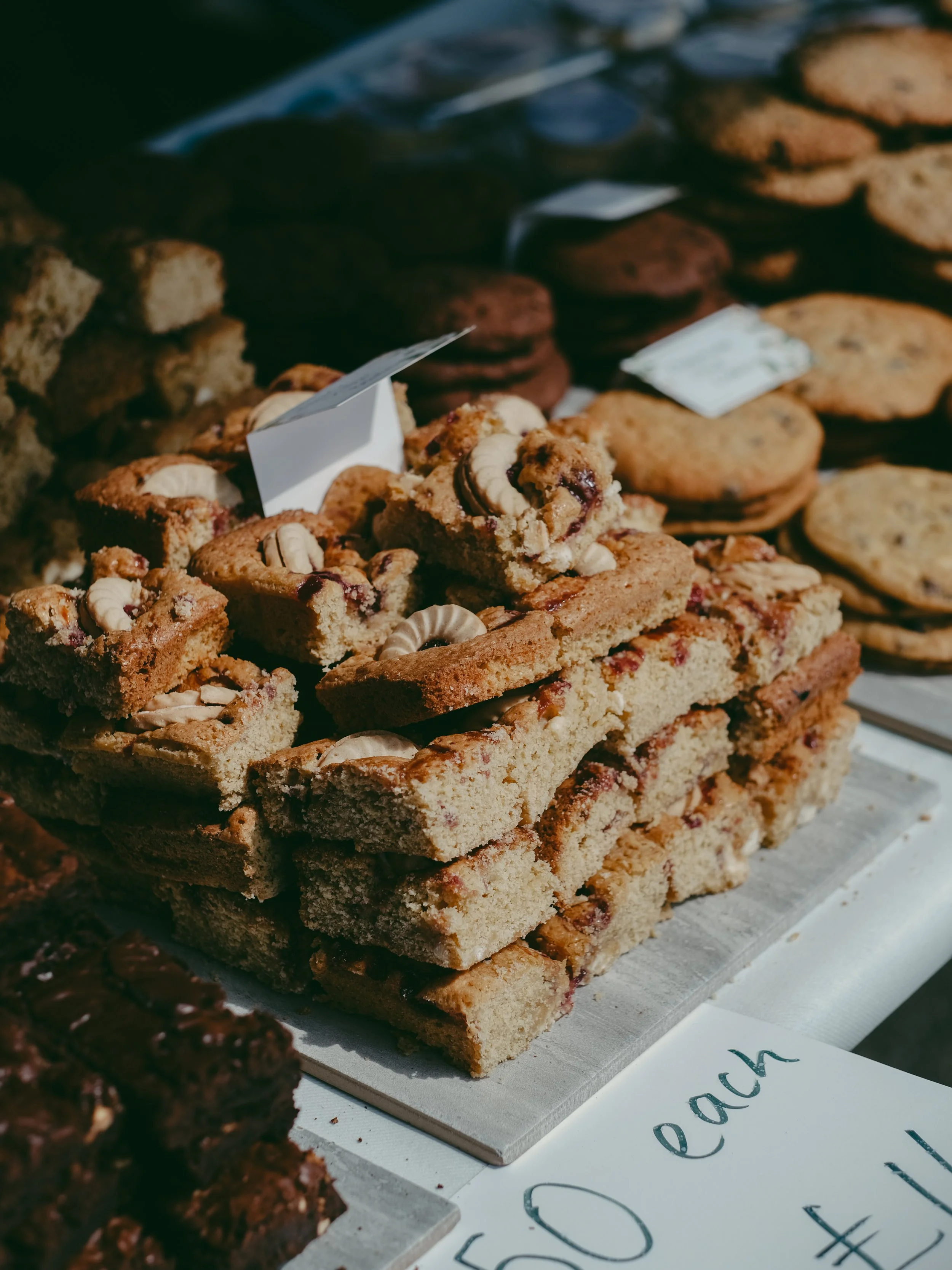 Stack of cookie bars with cashews and chocolate, displayed on a table at a bakery or market.