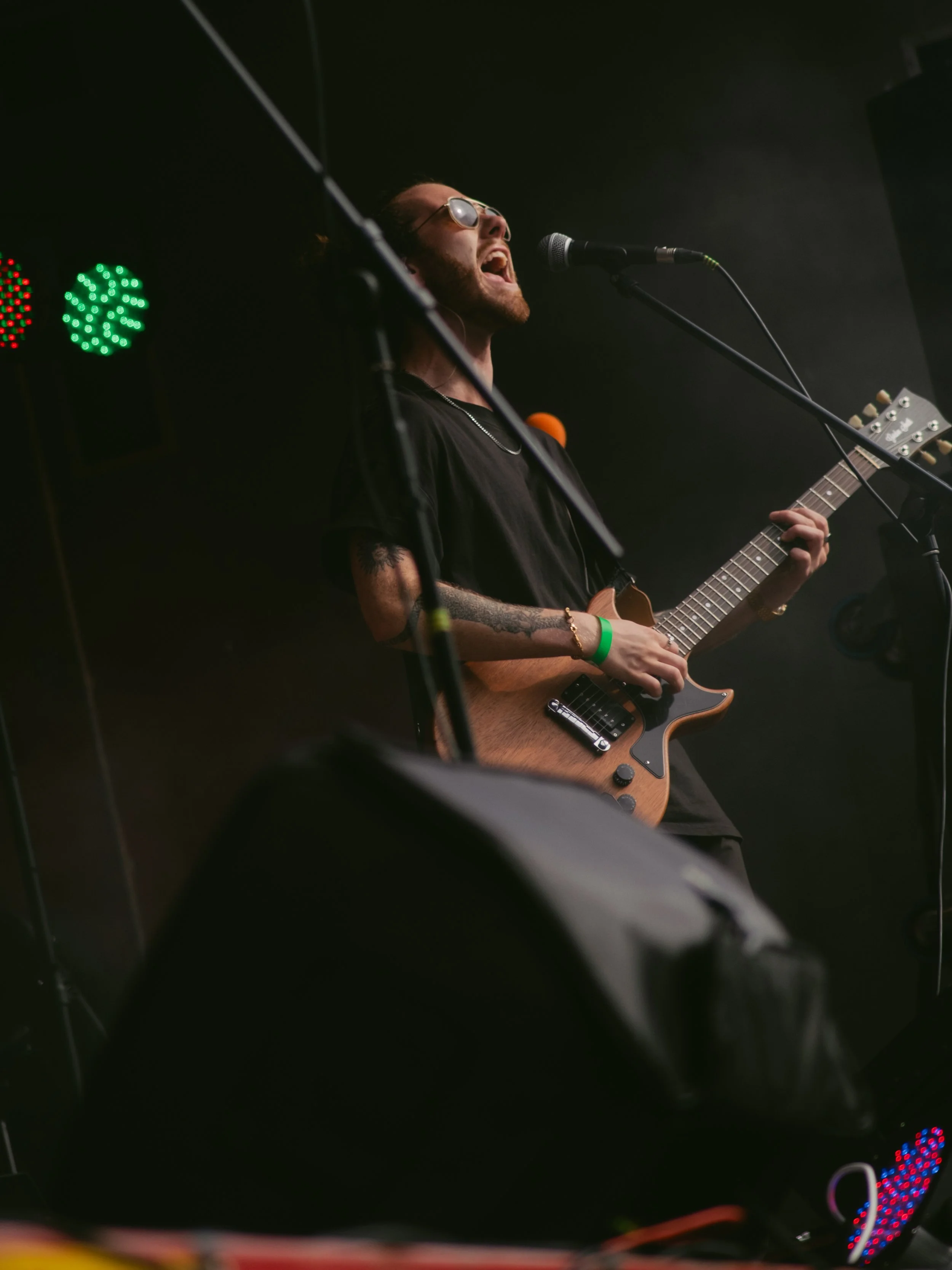 Musician singing and playing guitar on stage with dark background and stage lights.