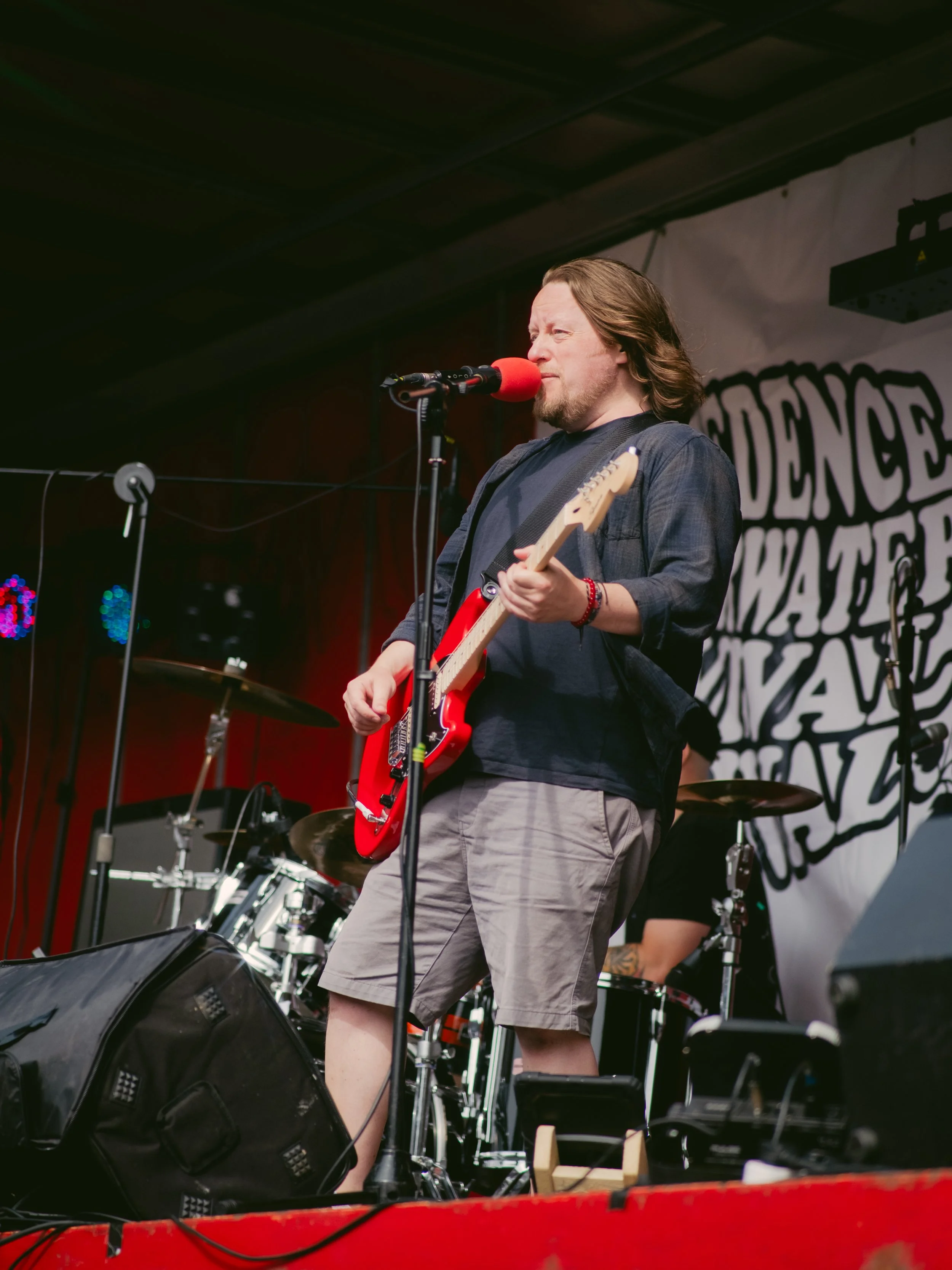 Man playing electric guitar and singing into a microphone on stage at a concert.