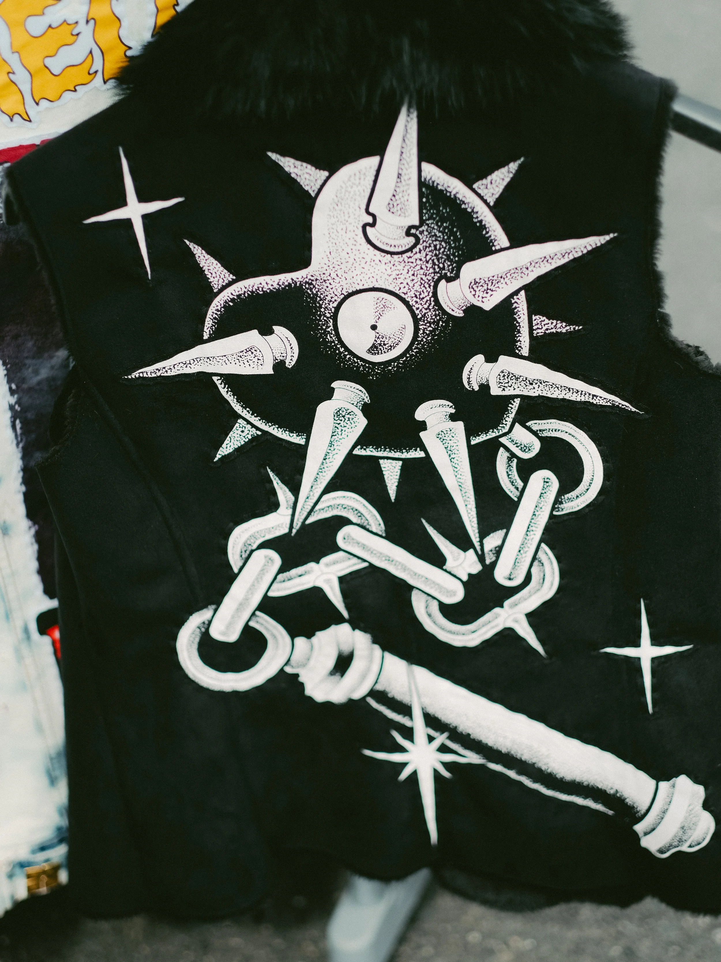 Black vest with white graphic design of a spiked mace and stars.