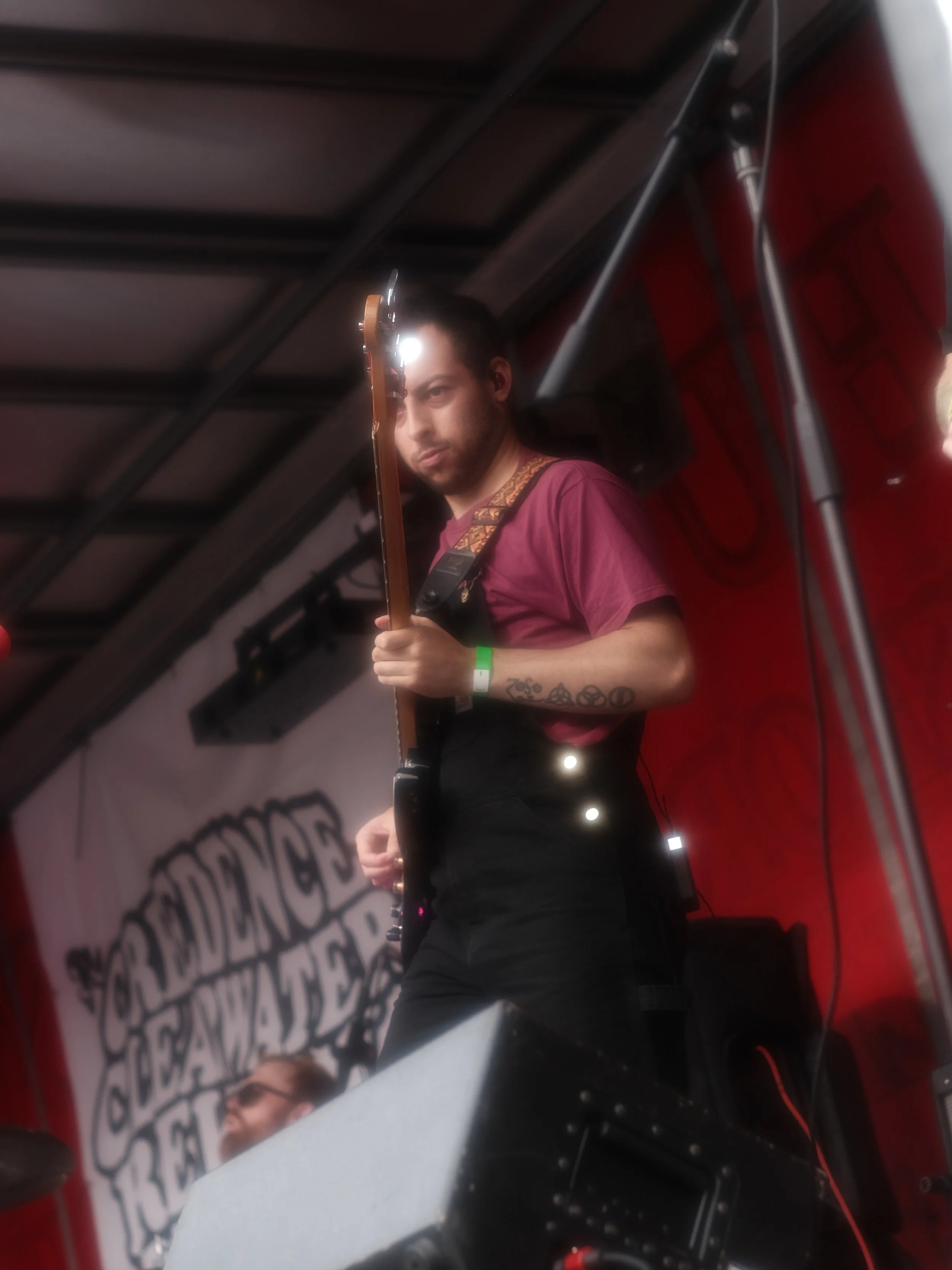 Musician playing an electric guitar on stage at a live performance, with a red backdrop and a banner that reads 'The End' in a stylized font.