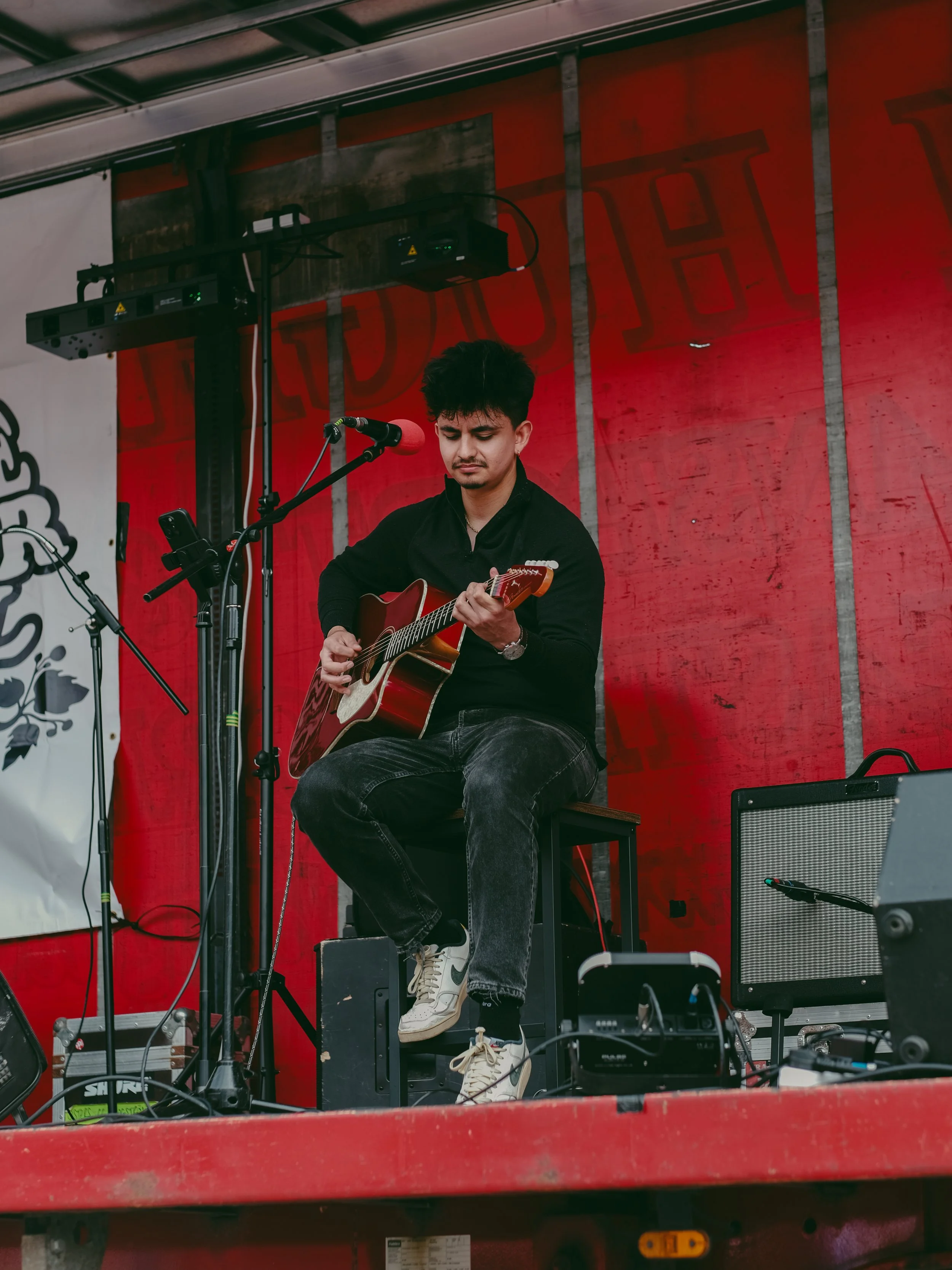 Young man playing an acoustic guitar on stage at an outdoor event.