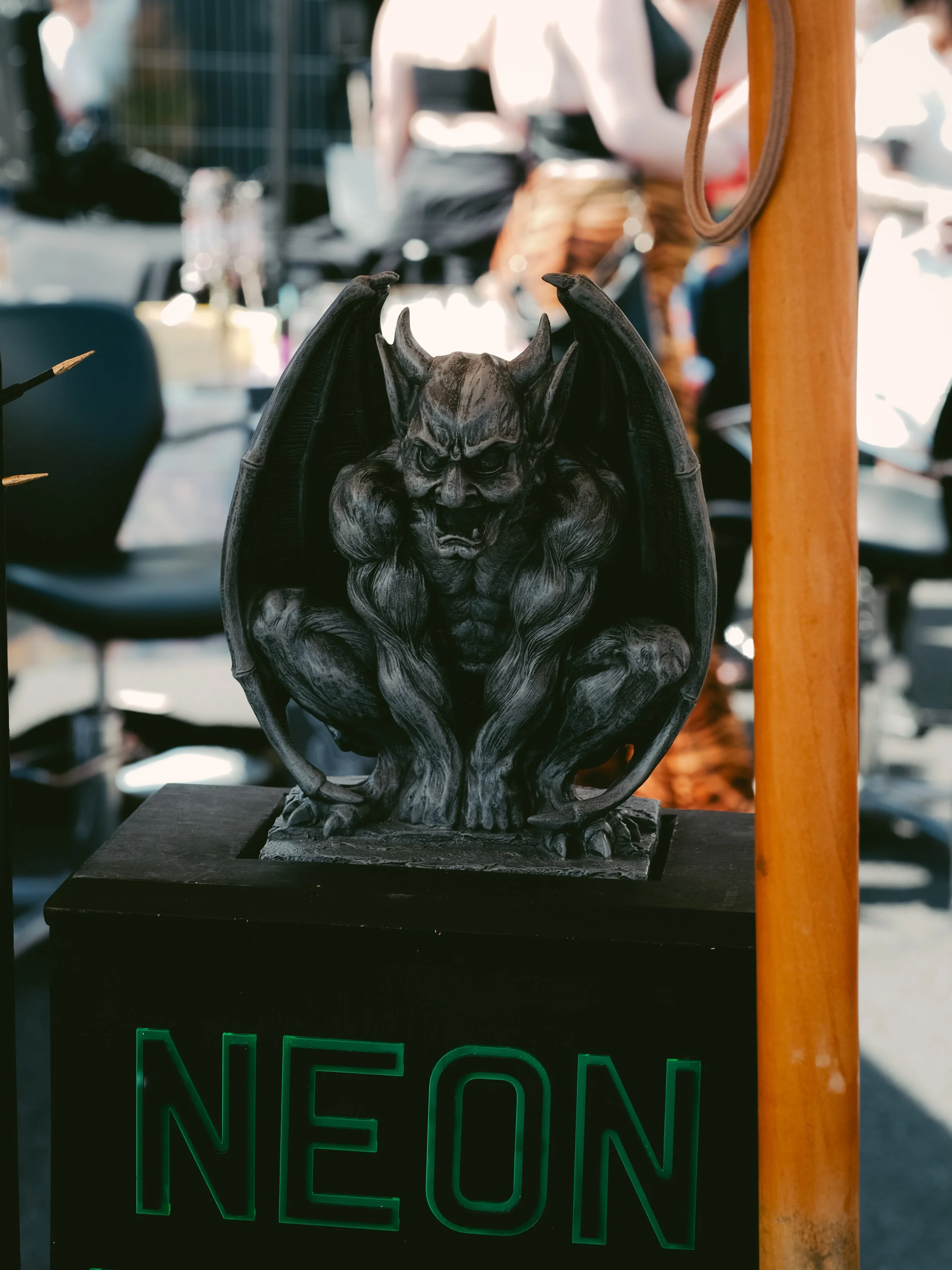 A black and gray sculpture of a demonlike creature with wings and horns, crouching on a black base with a neon green